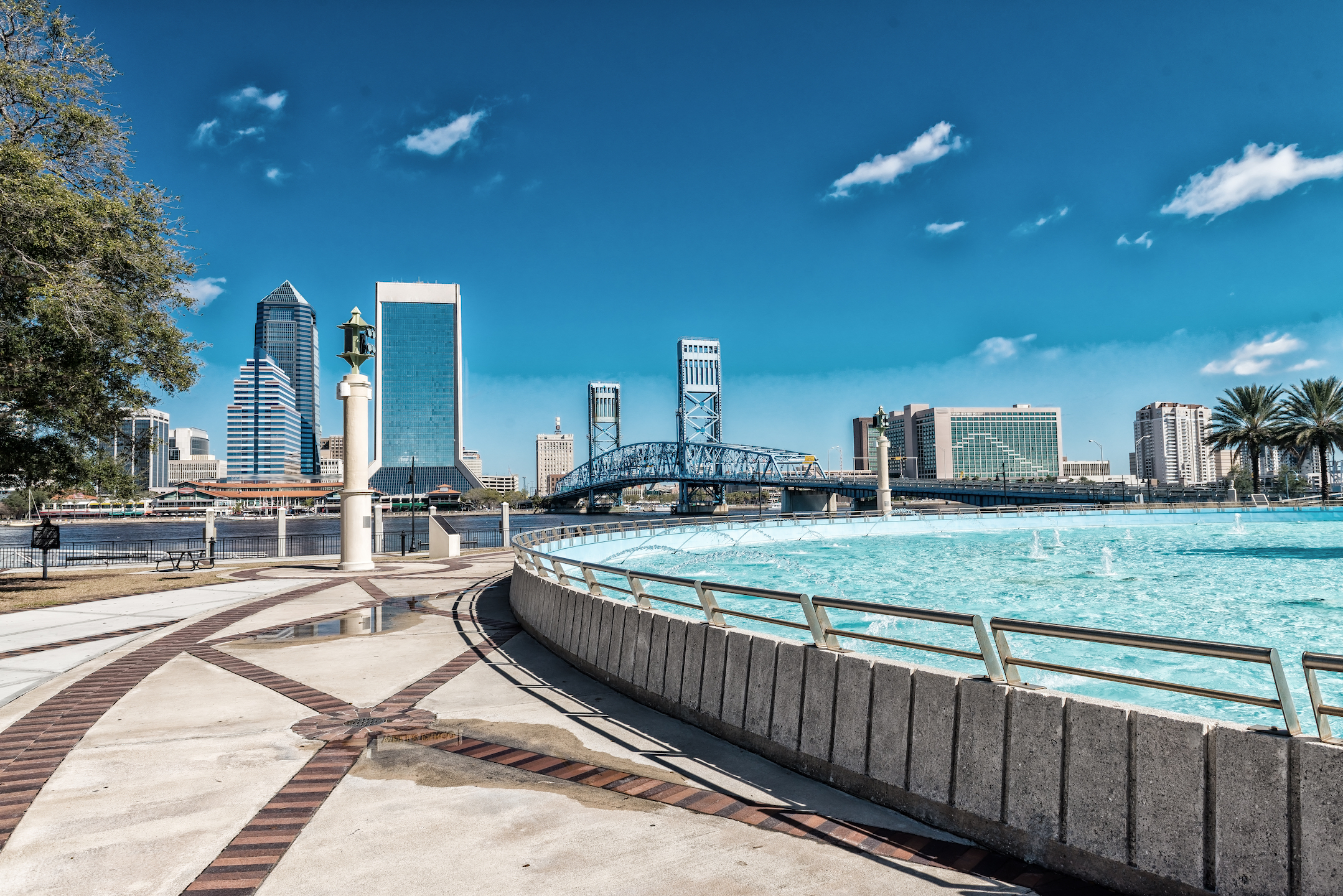 Skyline of downtown Jacksonville, Florida with the iconic blue Main Street Bridge and fountain in the foreground on a clear day.