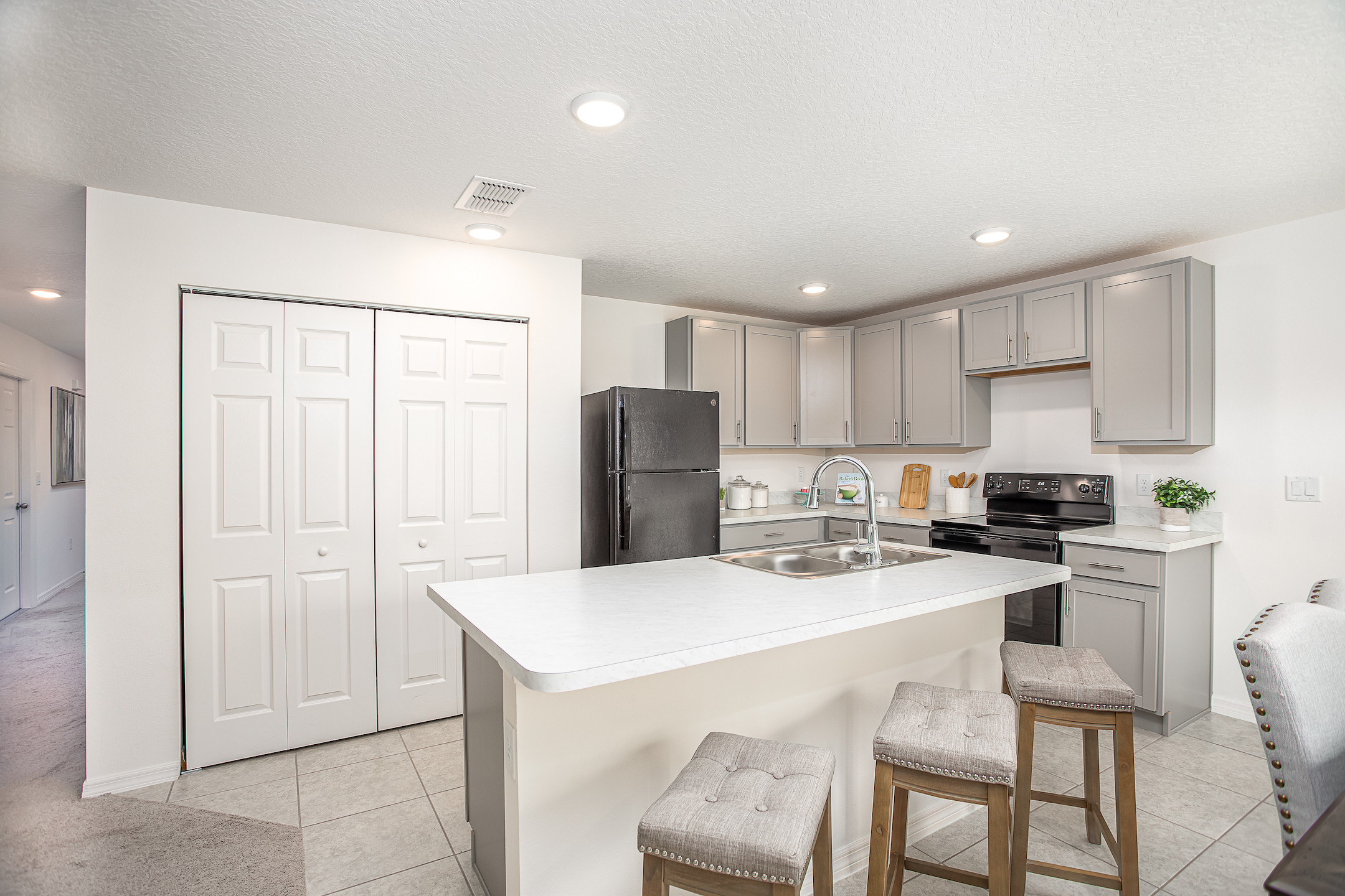 Modern kitchen with gray cabinets, black appliances, and a central island featuring a sink and bar stools.