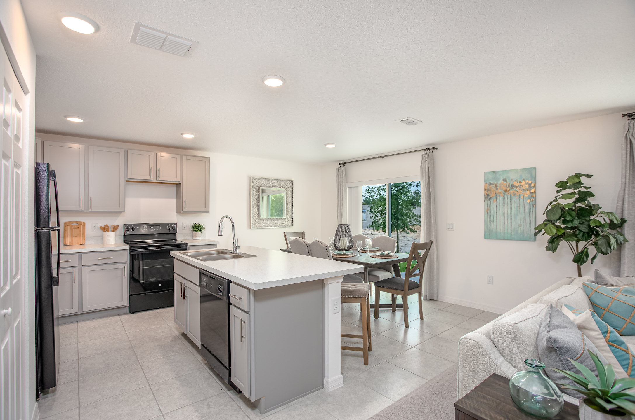 Modern kitchen with gray cabinets, a black stove, and a breakfast bar overlooking a cozy dining area with natural light.