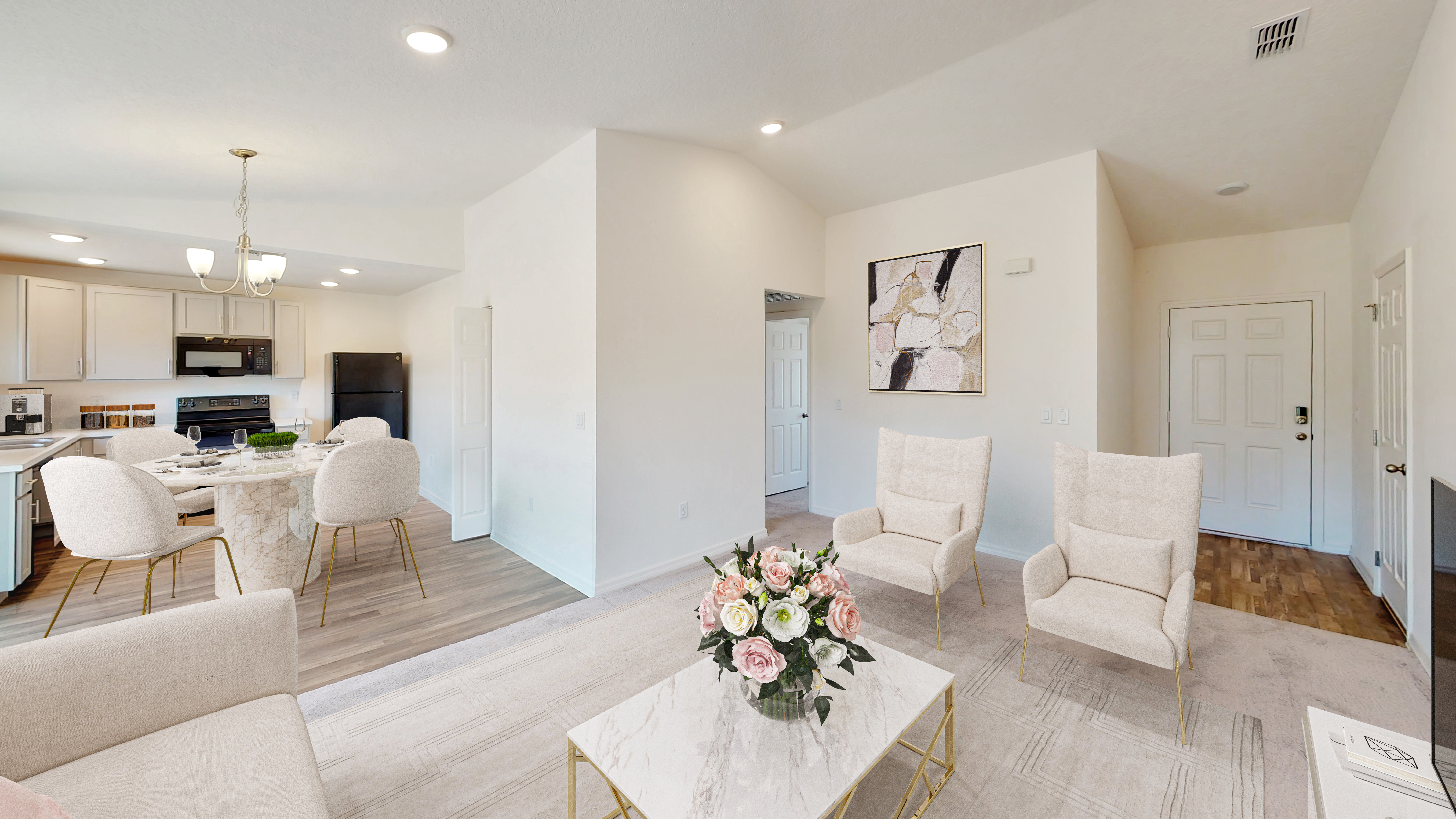 Modern open-concept living room and kitchen with elegant white furniture, floral centerpiece, and contemporary decor.