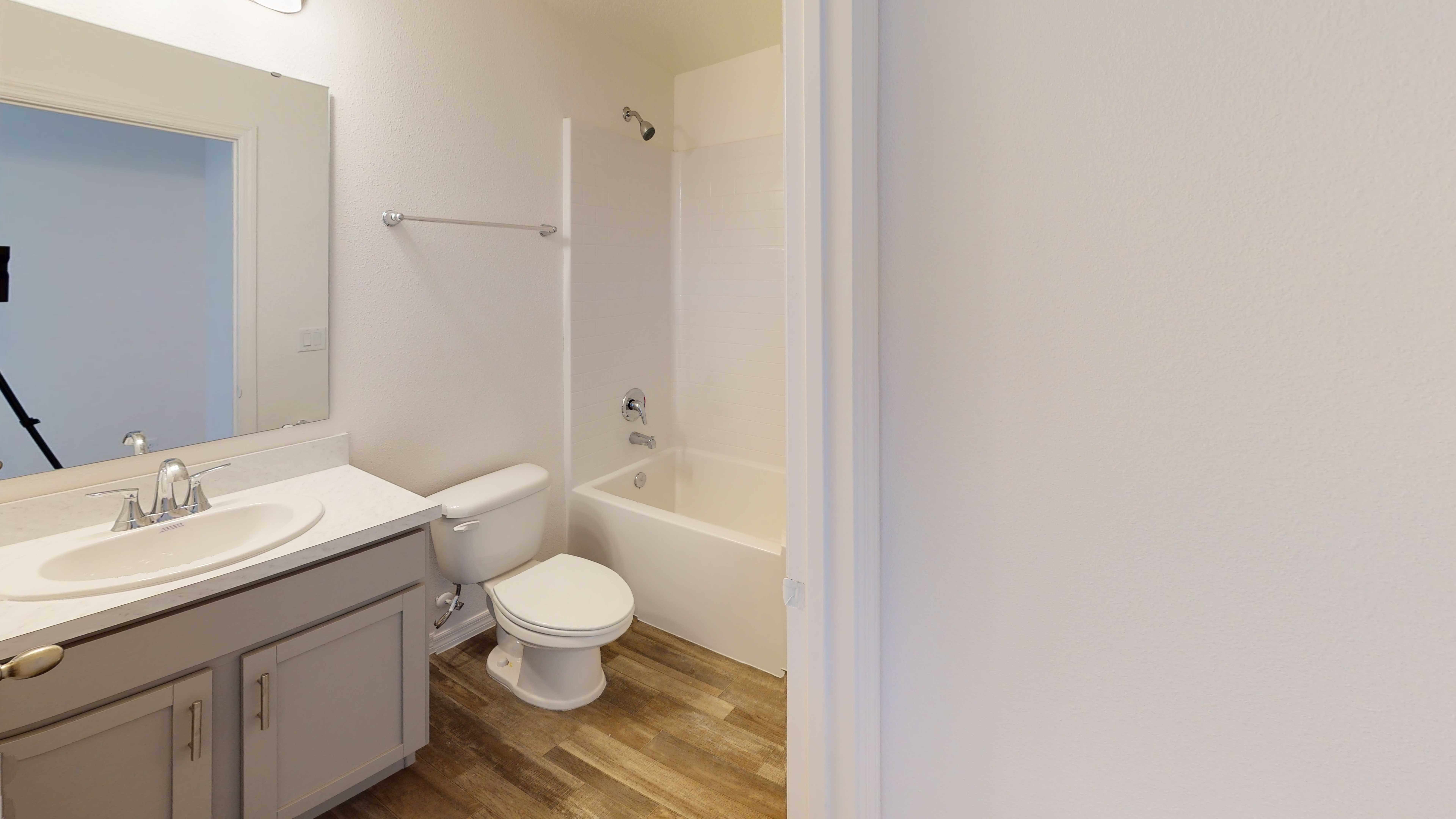"Modern bathroom with white fixtures, featuring a bathtub, toilet, sink with countertop, and wooden floor."