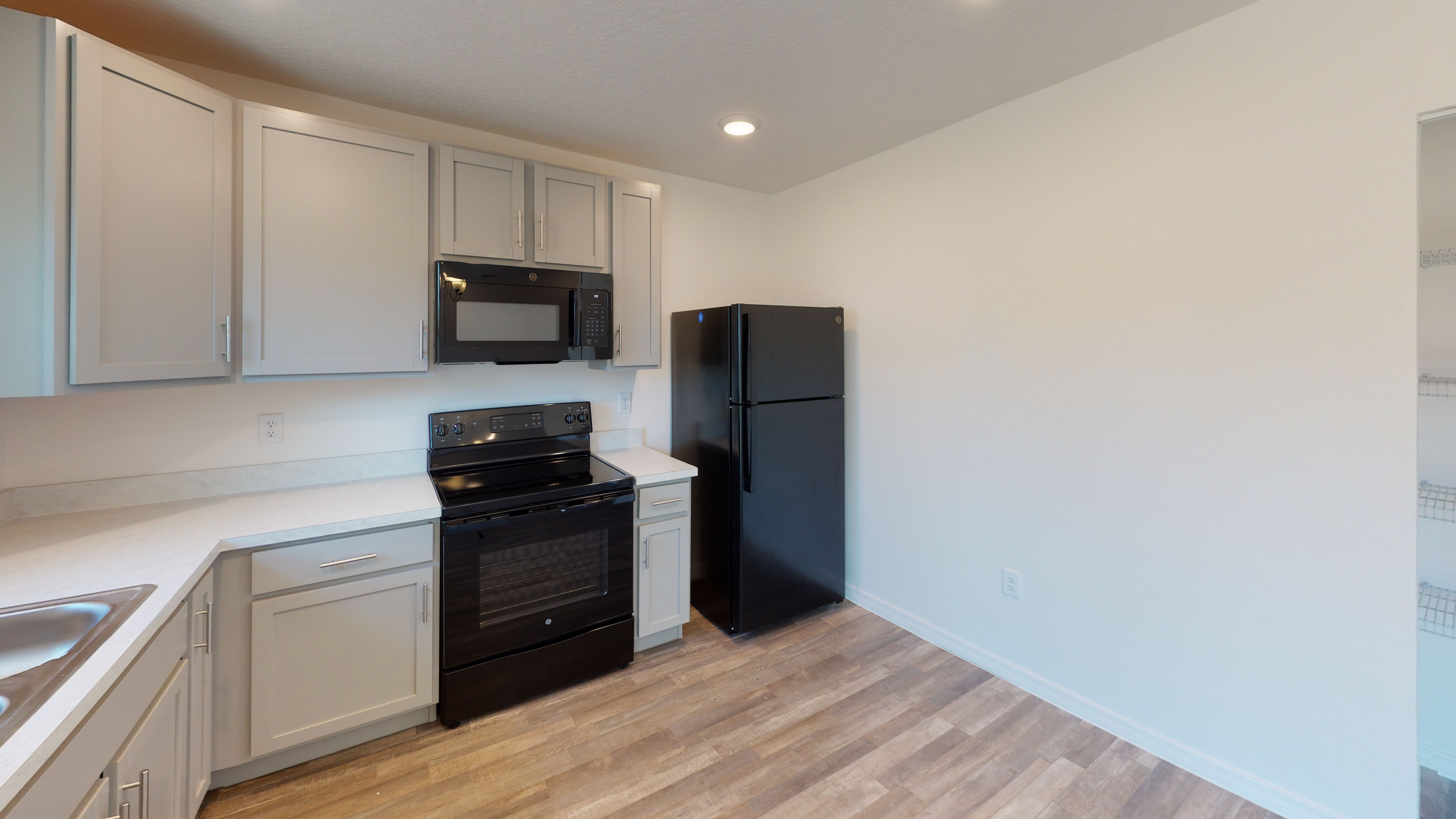 Modern kitchen with light cabinets, black appliances, and wood flooring.