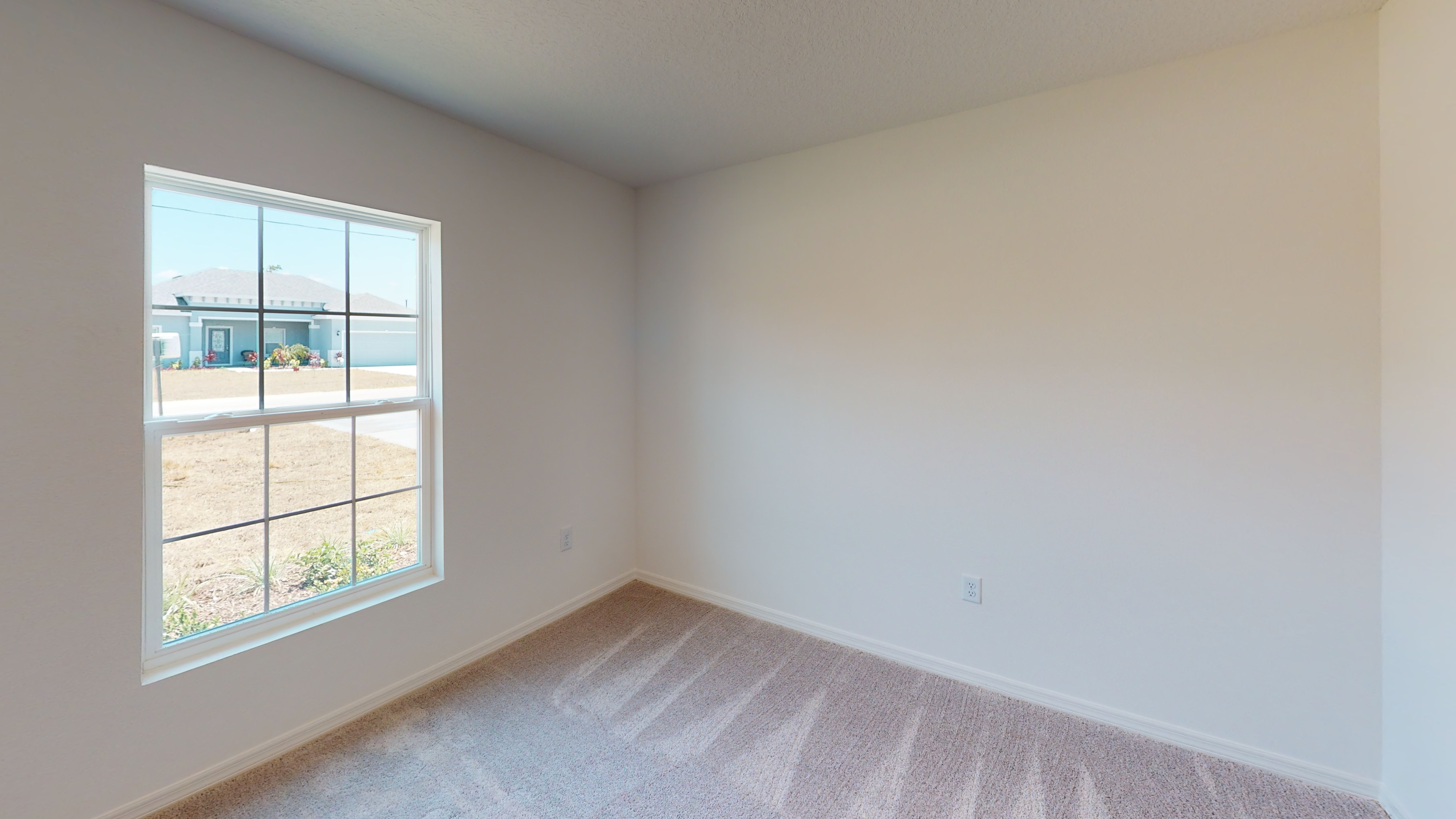 Bright, empty room with beige carpet and a large window showing an exterior suburban view.