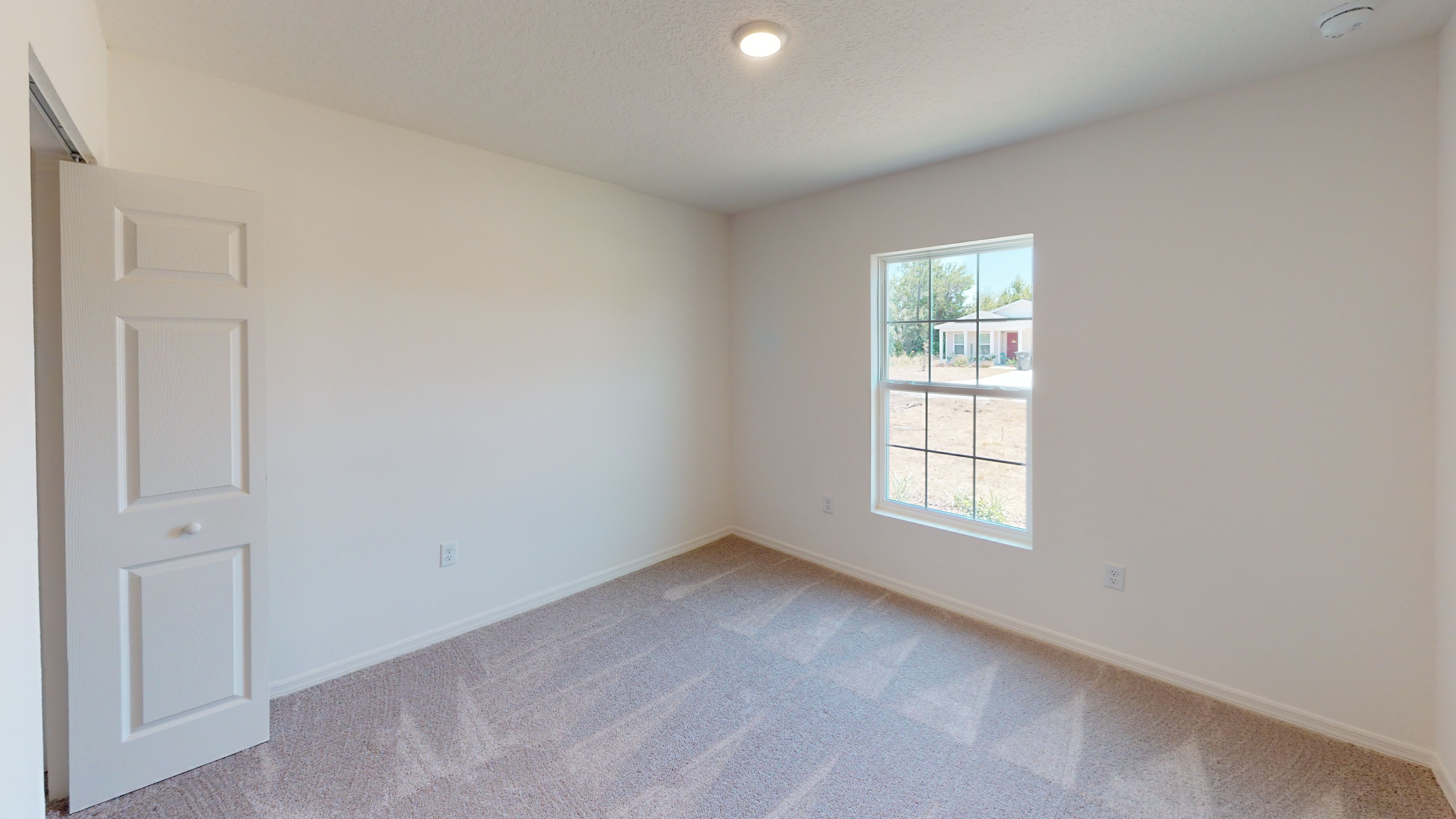 "Bright, empty room with fresh carpet, white walls, and a large window overlooking a suburban street."