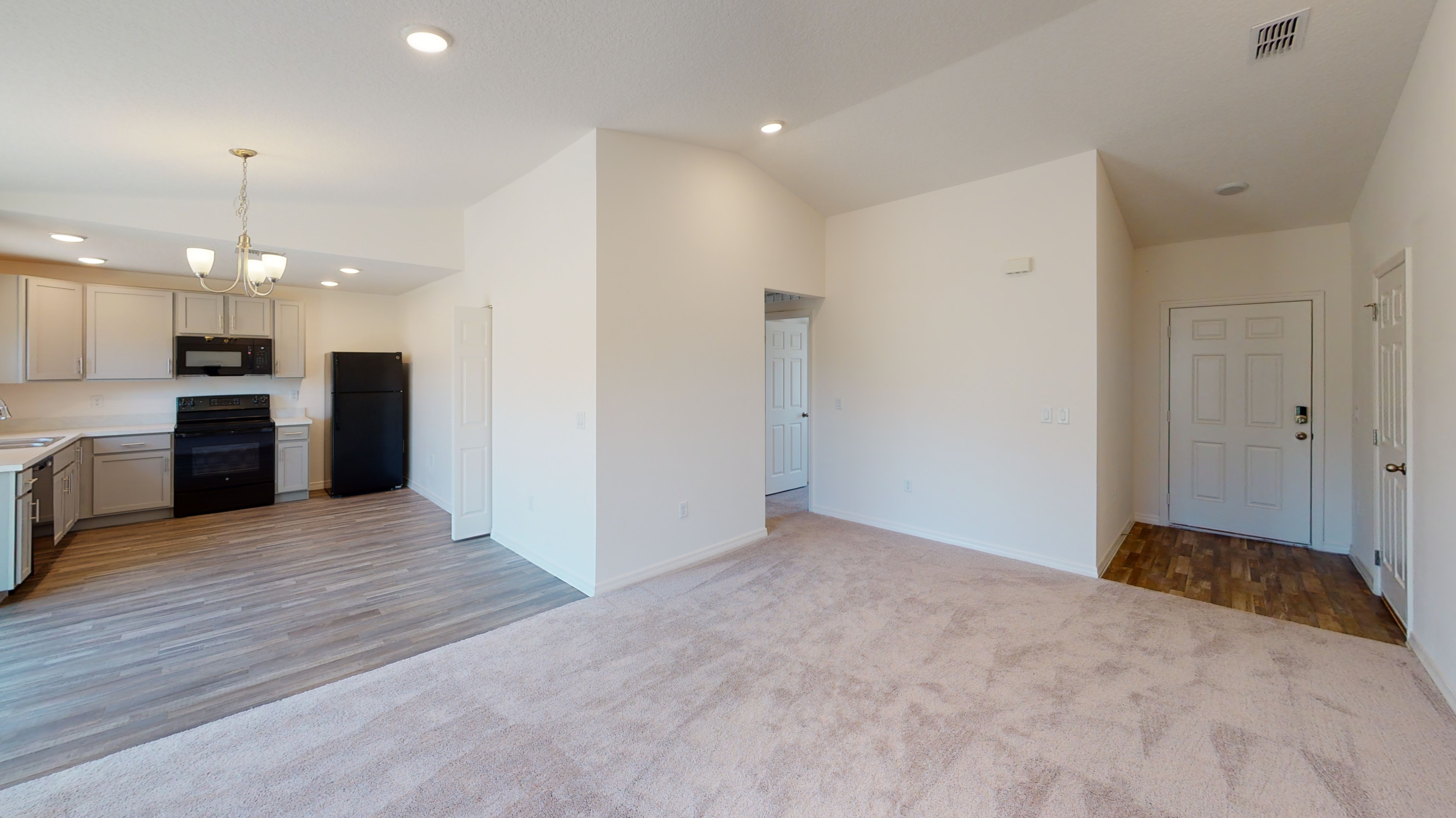 "Spacious open-plan living room and kitchen area with modern appliances and hardwood flooring leading to a carpeted space."