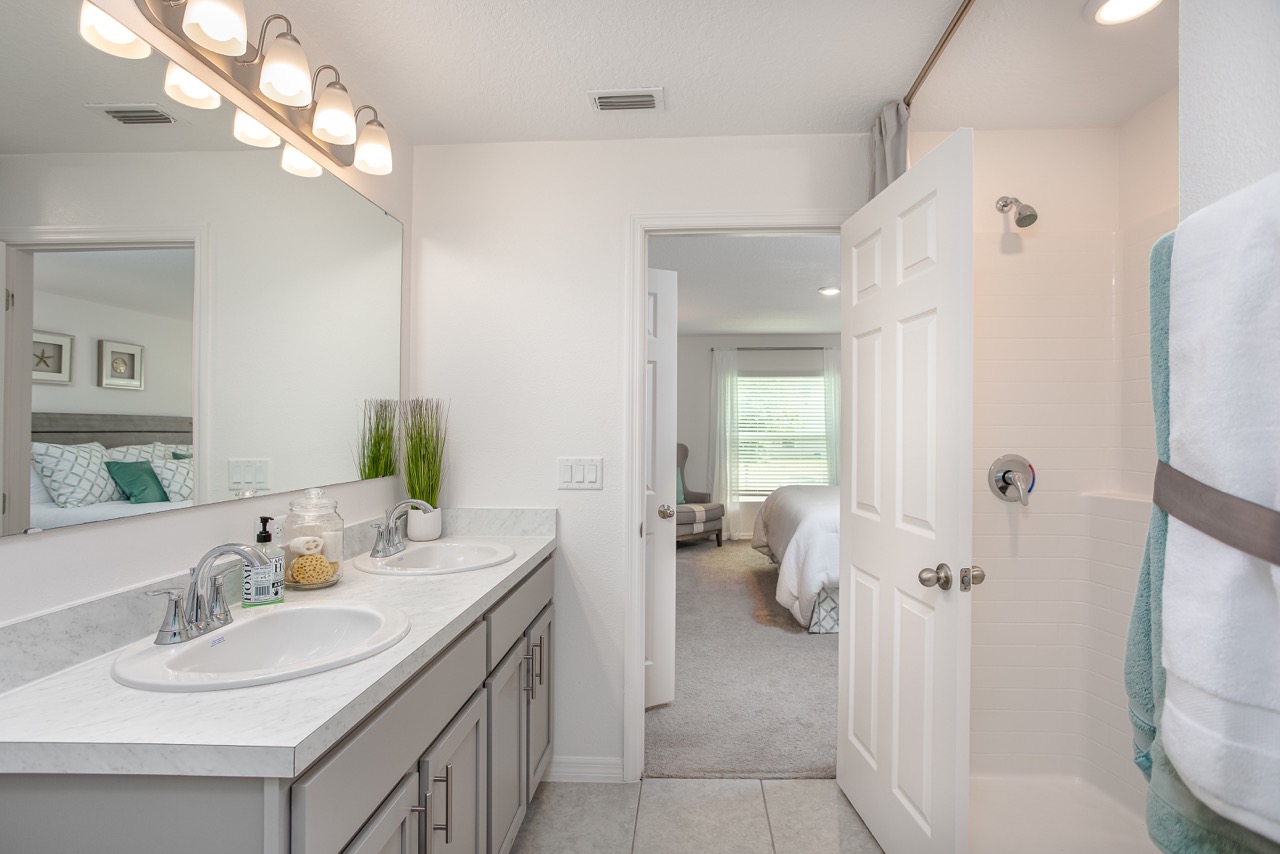 Modern double-sink bathroom with marble countertops, stylish lighting, and adjacent view into a bright bedroom.