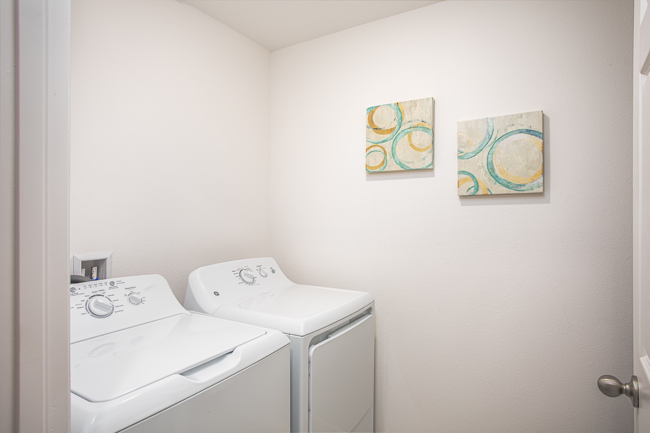 A modern laundry room with white washing machine and dryer, featuring abstract art on the walls.