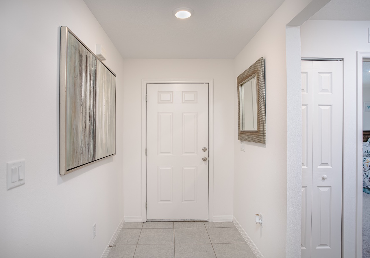 Bright, modern hallway with white walls, a closed door, abstract artwork, and a mirror reflecting light.