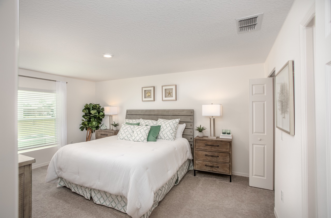 Modern bedroom with a cozy white bed, wooden nightstands, and decorative green pillows, lit by natural light from a window.