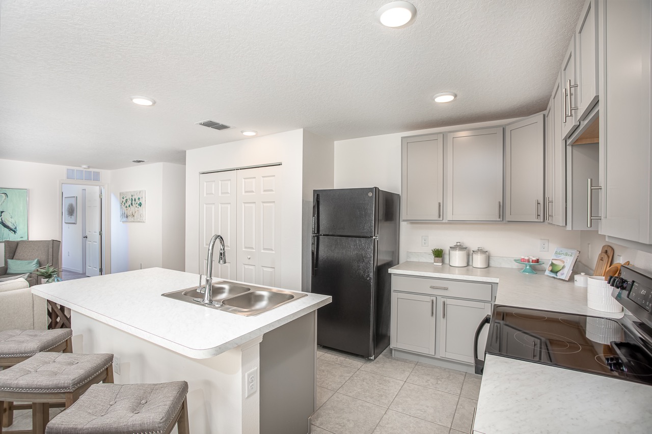 Modern kitchen with gray cabinets, black appliances, and a white countertop featuring a double sink and bar seating.