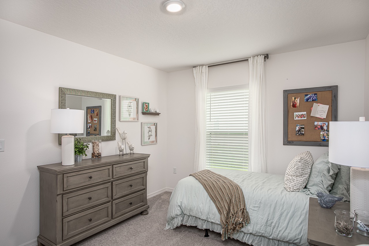 Cozy bedroom with a soft blue bedspread, gray dresser with a mirror, and a bulletin board on the wall.