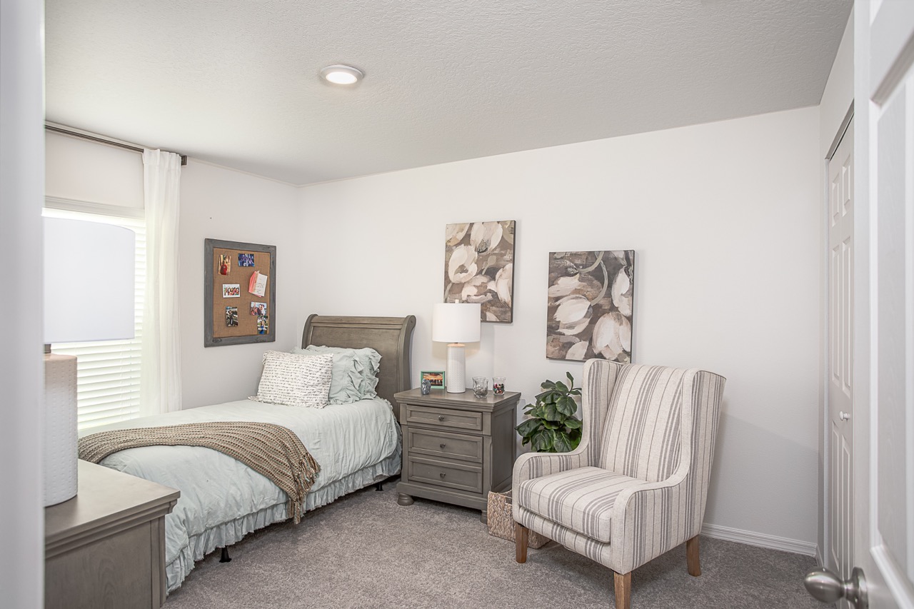 "Cozy bedroom with a neatly made bed, gray nightstand, striped armchair, and elegant wall art, creating a serene and inviting atmosphere."