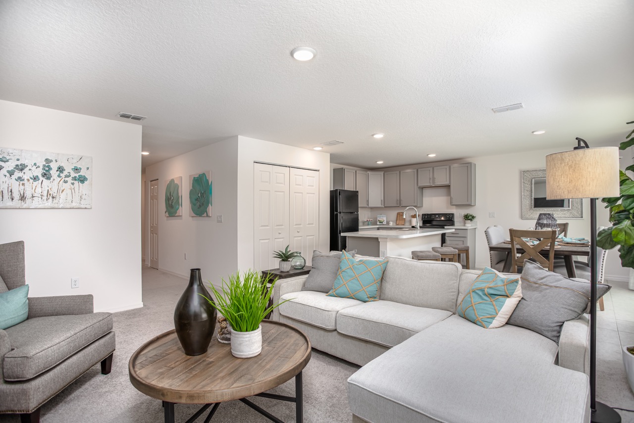 Modern open-plan living room with gray sectional, wooden coffee table, and a contemporary kitchen and dining area.