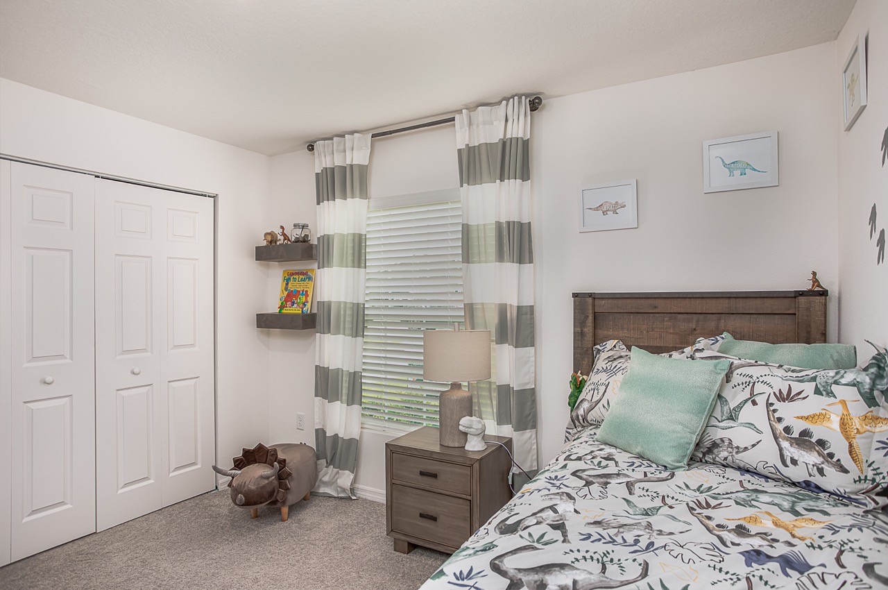 Cozy dinosaur-themed kids' bedroom with striped curtains, bookshelf, and decorative bedspread.
