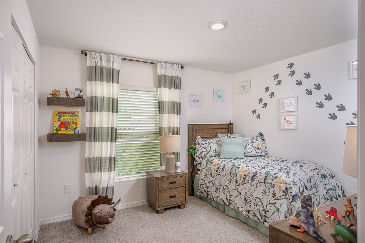 Children's dinosaur-themed bedroom with wall art, dinosaur figurines, and a colorful bedspread.