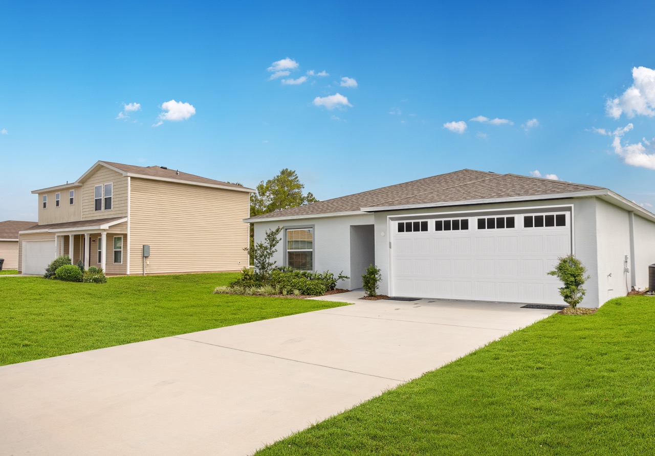 Alt tag: "Modern suburban homes with well-maintained lawns under a clear blue sky."