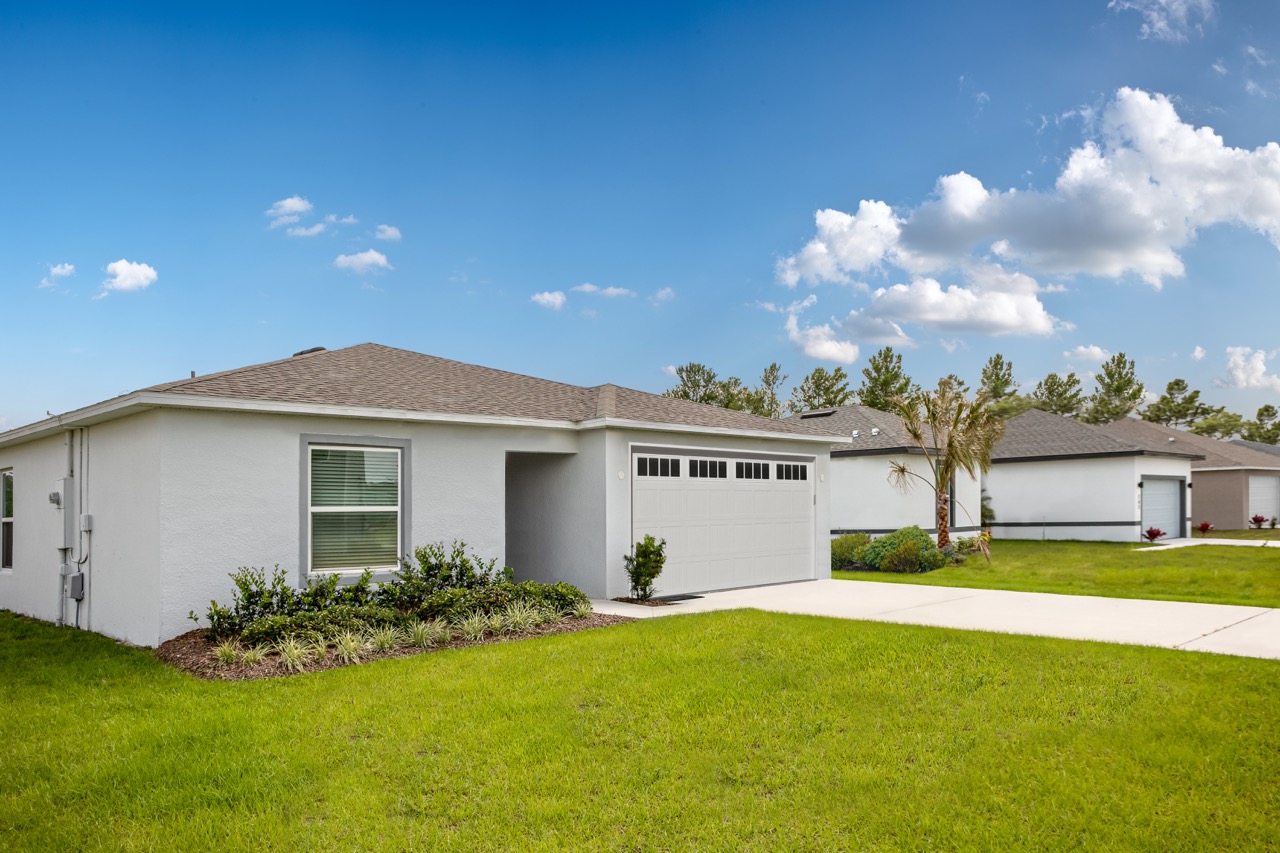 Single-story modern white house with a two-car garage and manicured lawn under a clear blue sky.