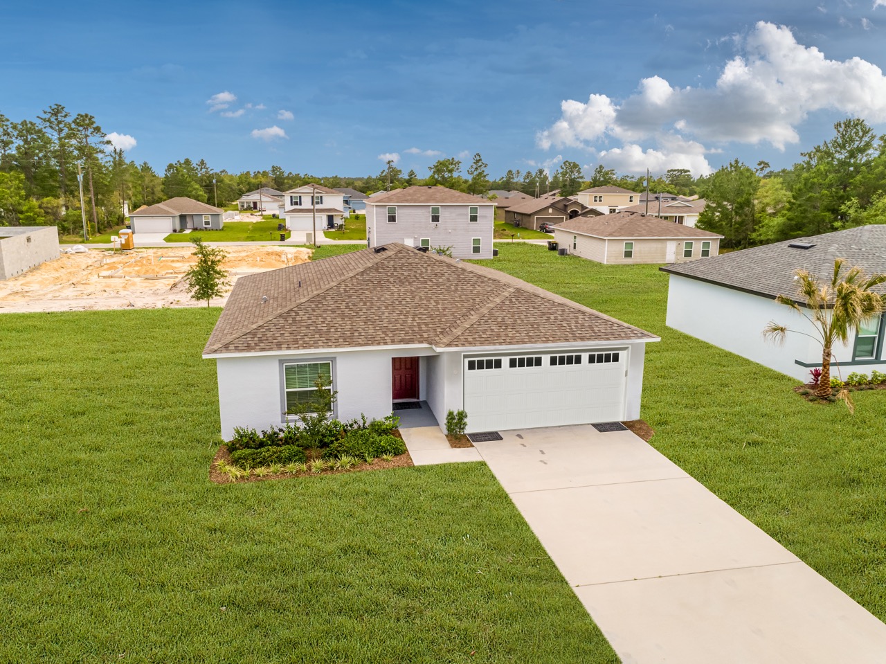 Aerial view of a modern single-story home with a two-car garage surrounded by lush green grass in a suburban neighborhood.