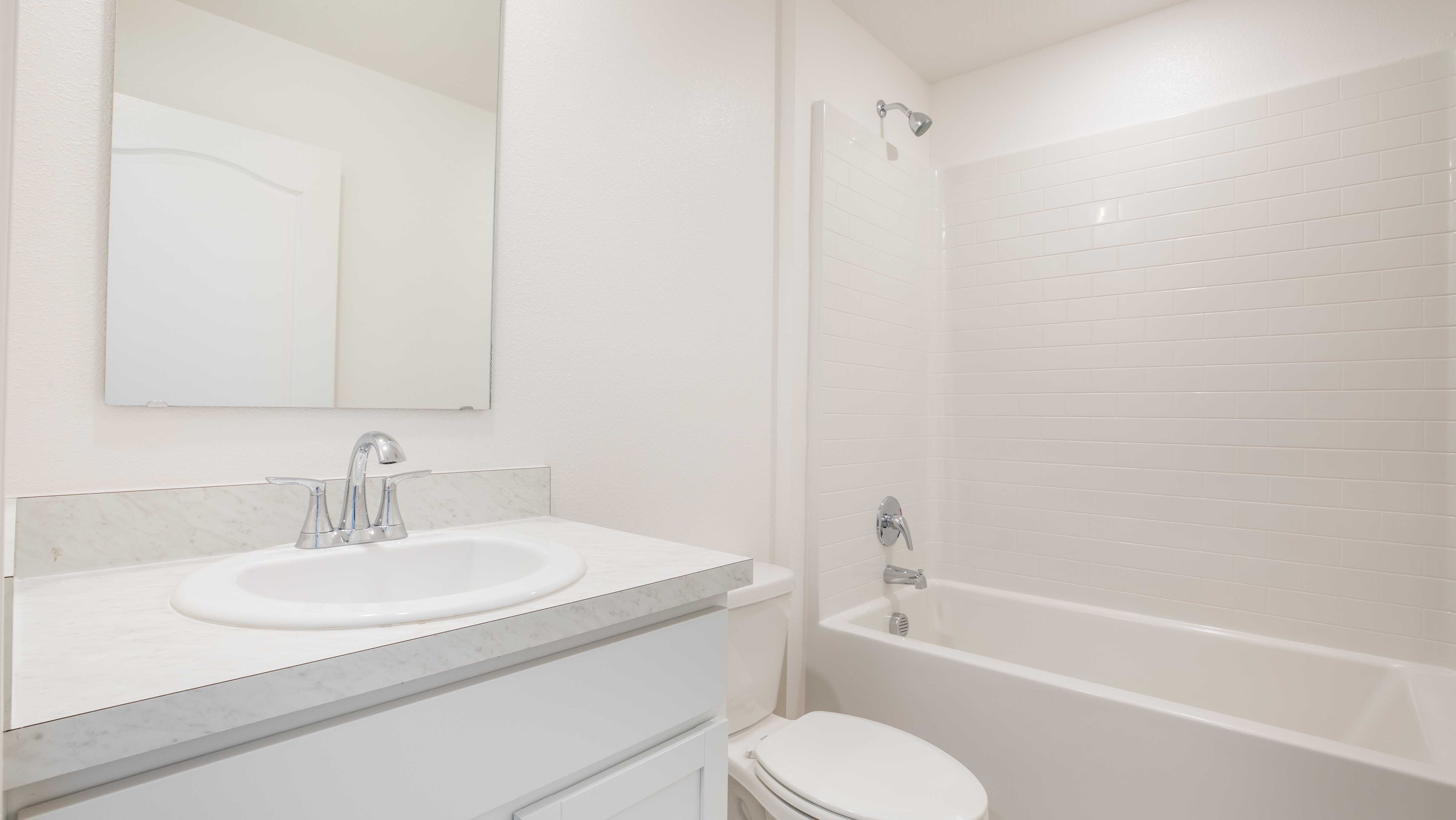 Bright, modern bathroom featuring a white tub with tile backsplash, toilet, and a sink with a mirror and chrome faucet.