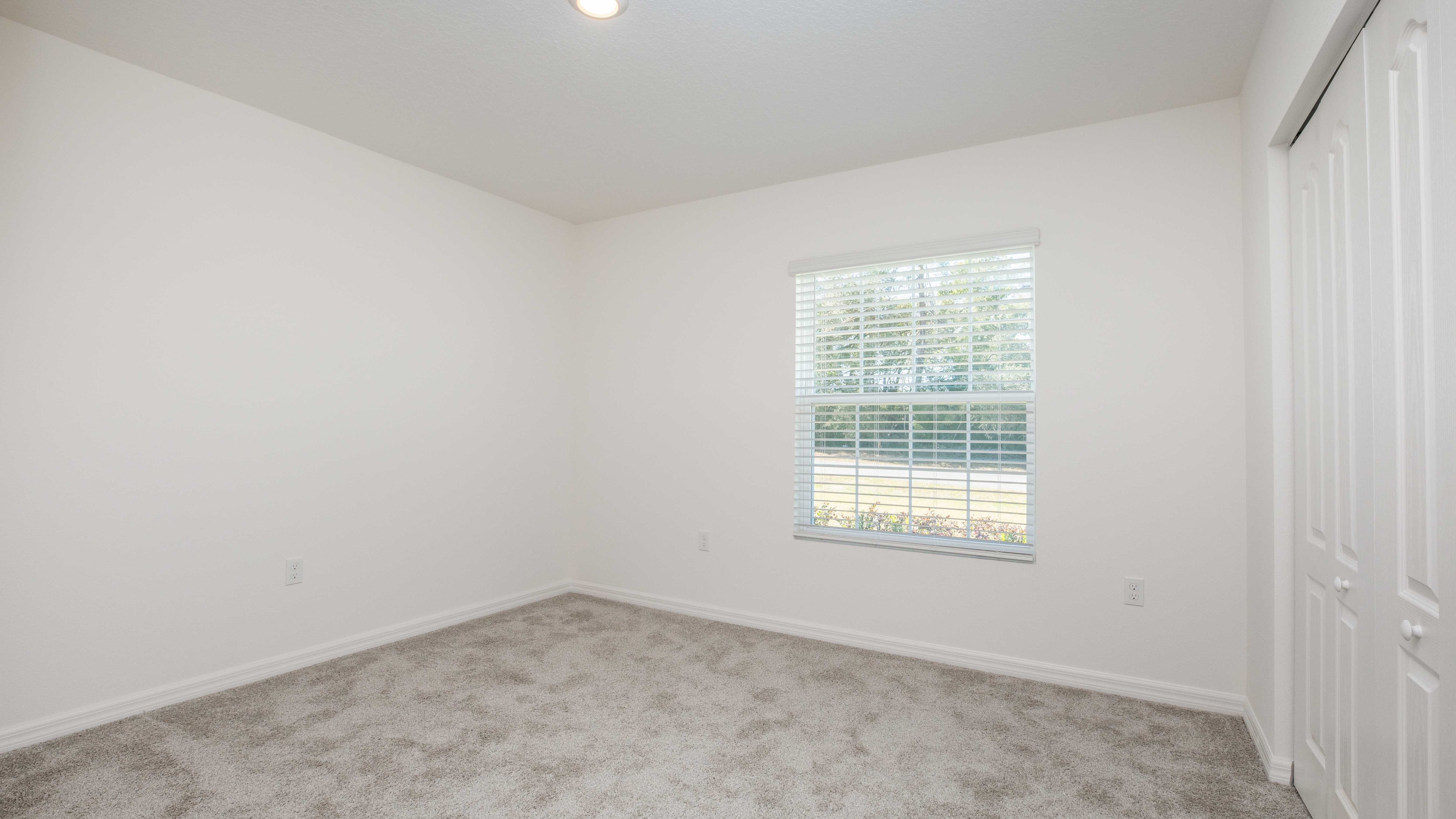 Empty white-walled room with carpet flooring, a window with blinds, and a closed closet door.