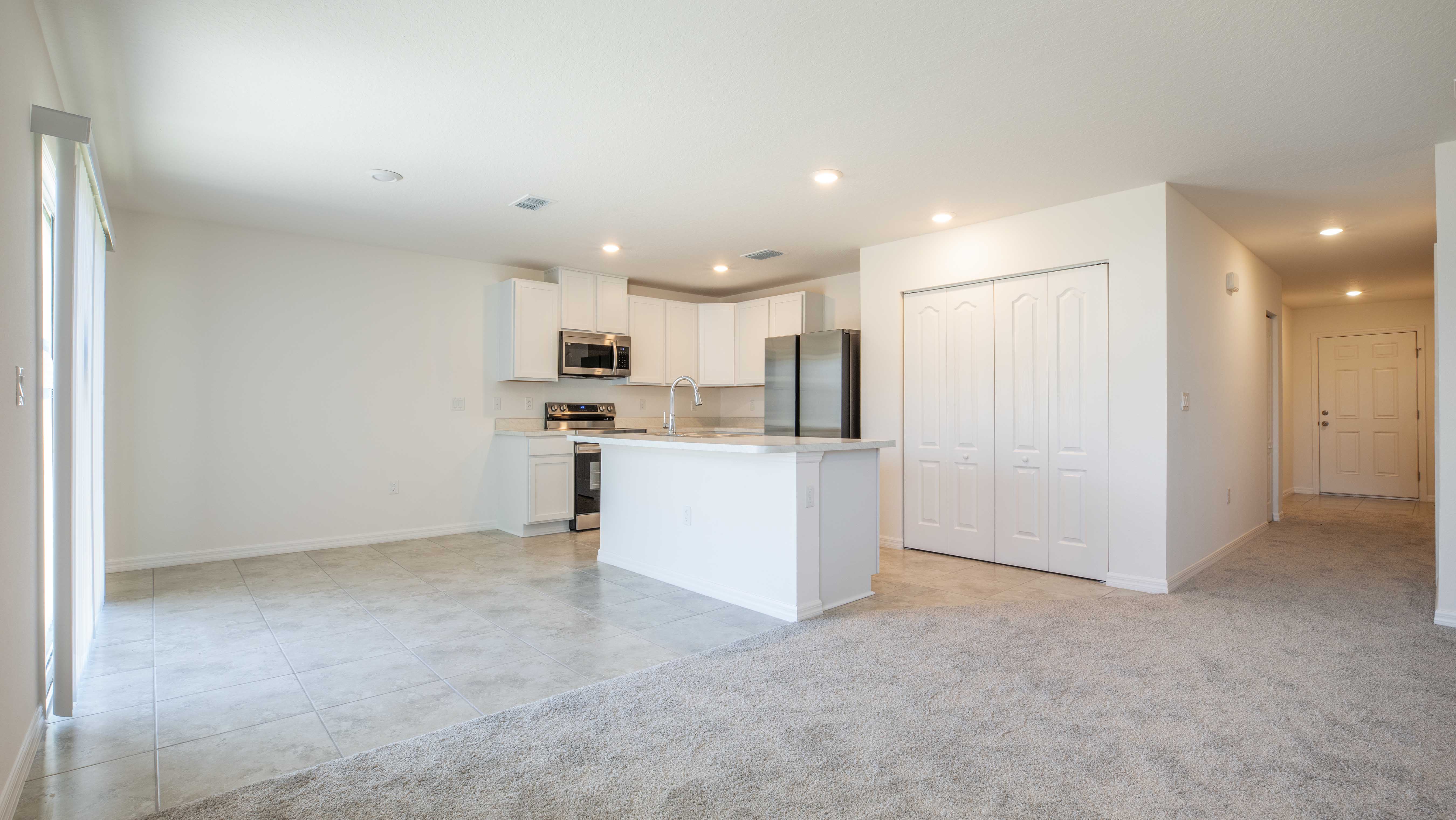 Modern kitchen interior with white cabinets, stainless steel appliances, and an island in an open-concept space.