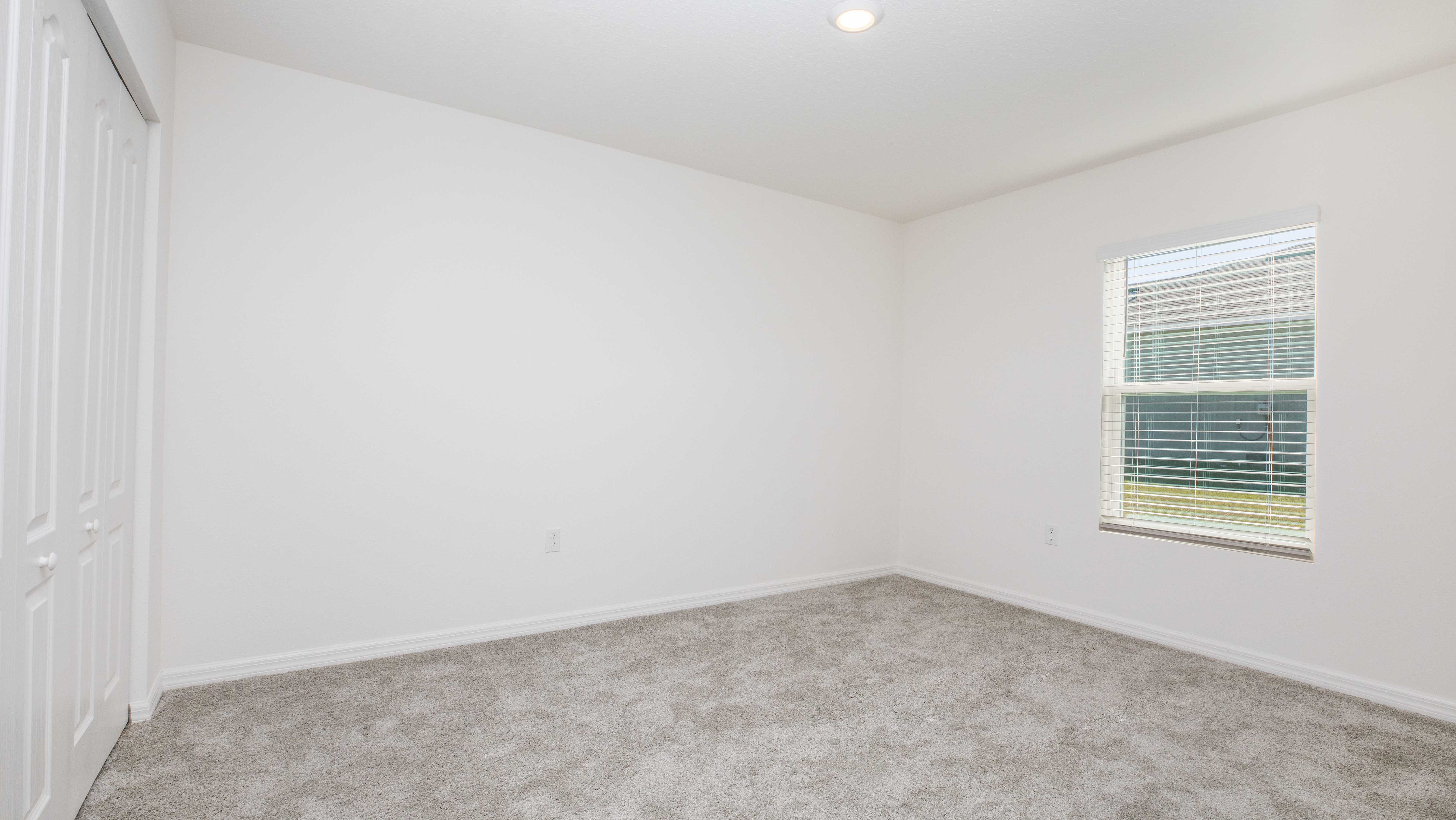 "Empty room with white walls, carpeted floor, and a window with blinds letting in natural light."