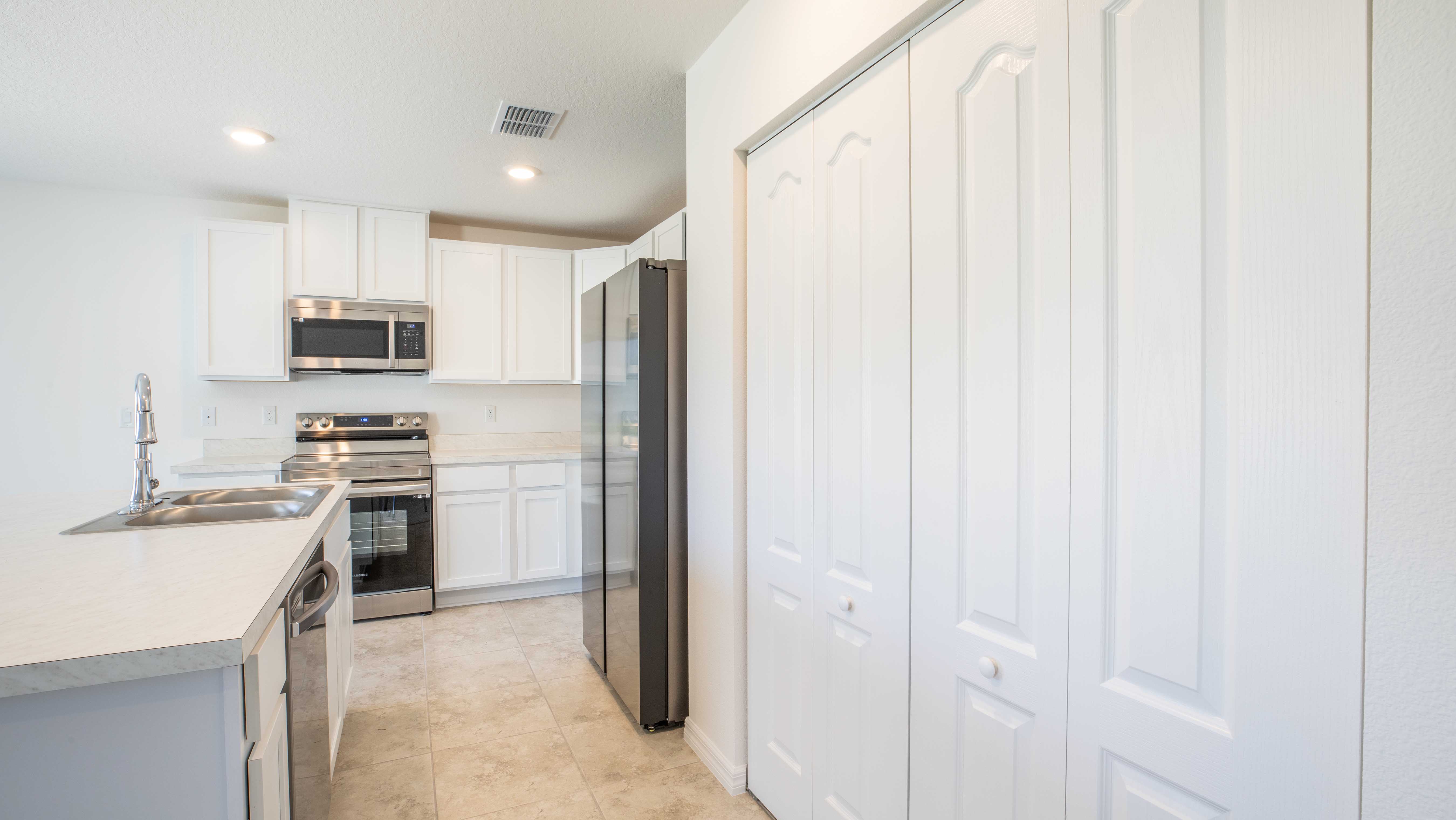 Modern white kitchen with stainless steel appliances, including a refrigerator, microwave, and oven, featuring ample cabinetry and a large sink.