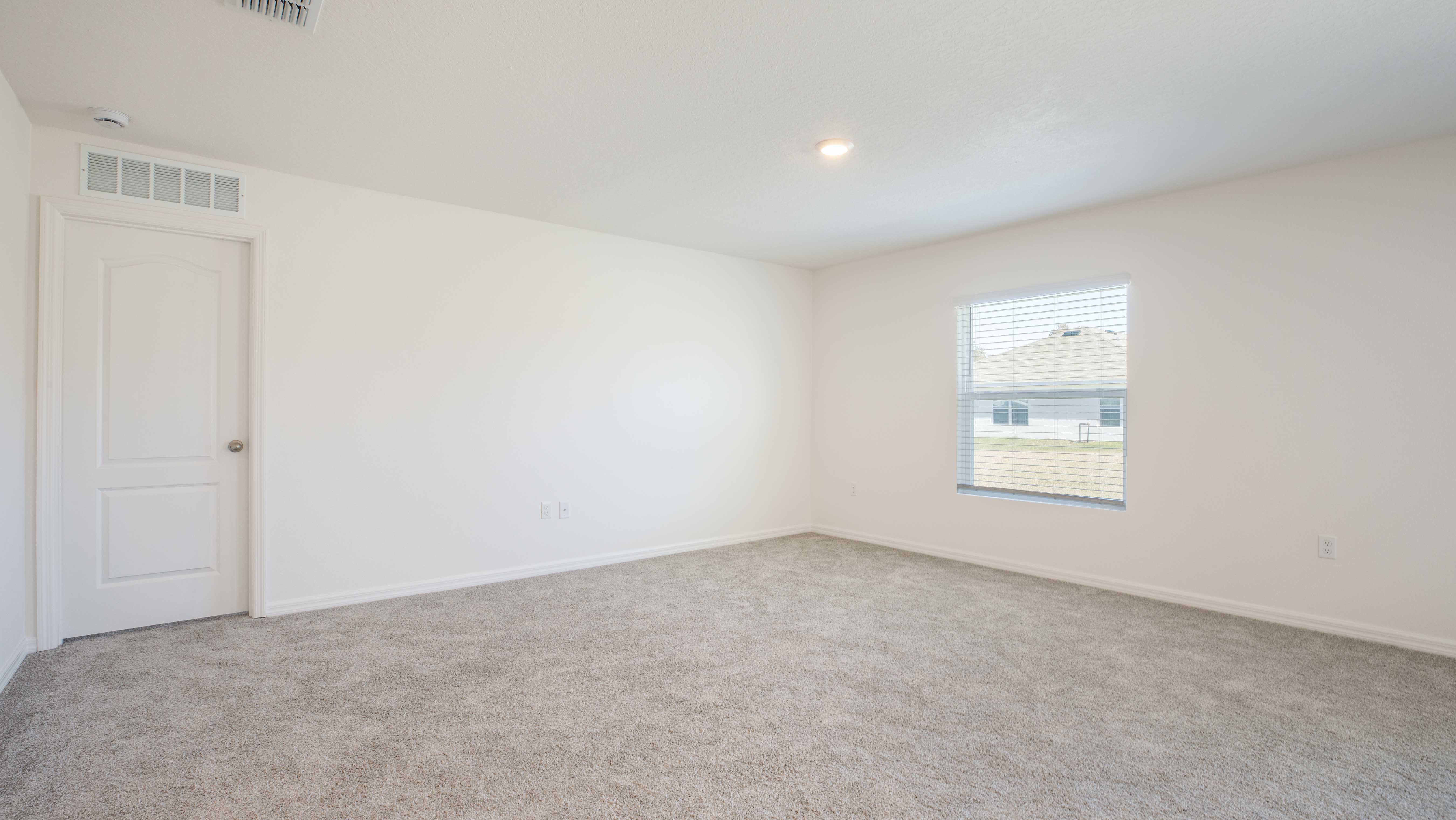 Empty, bright carpeted room with a window and a white door.