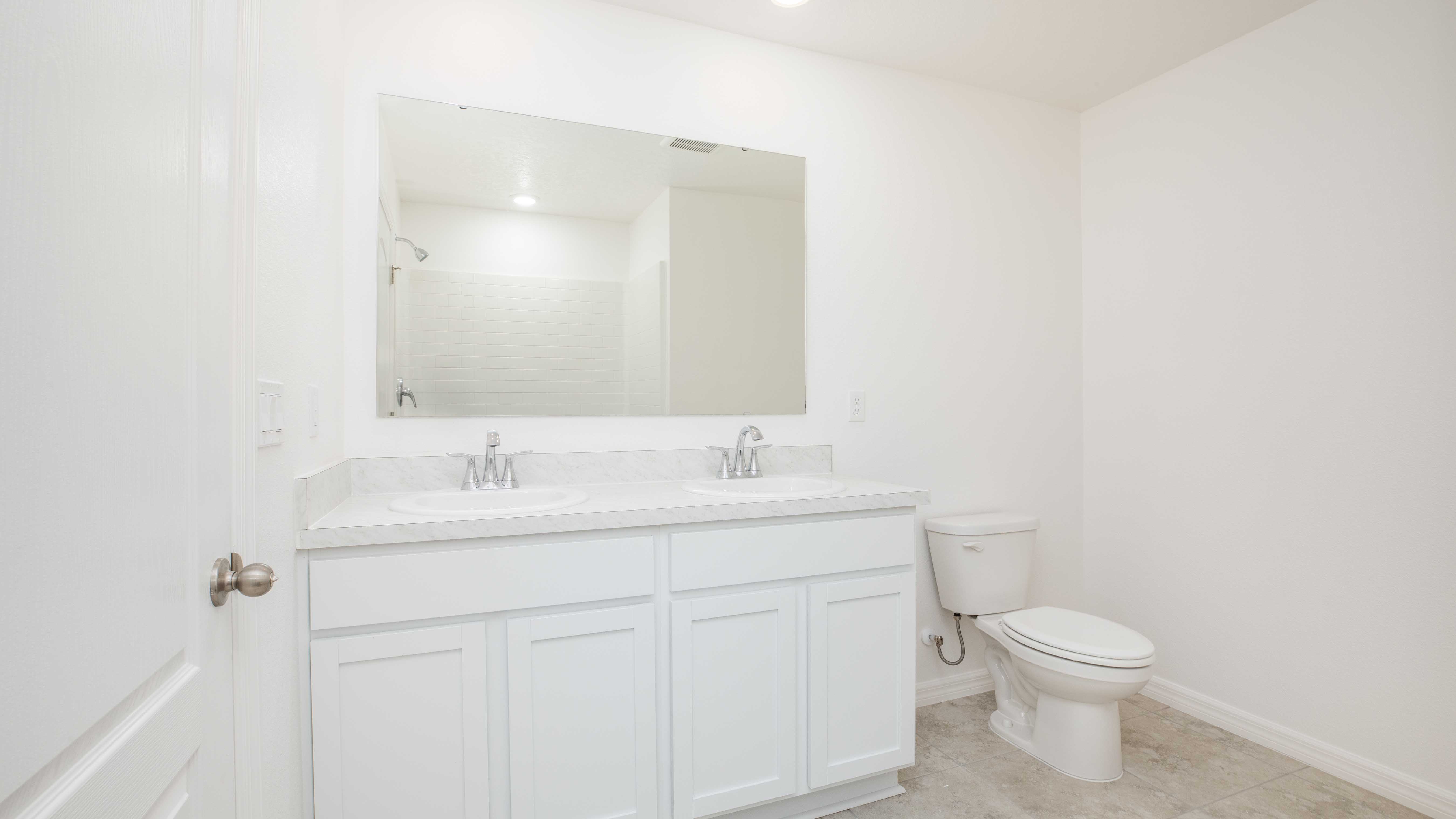 Bright and clean white bathroom with a large mirror, double sink vanity, and toilet.