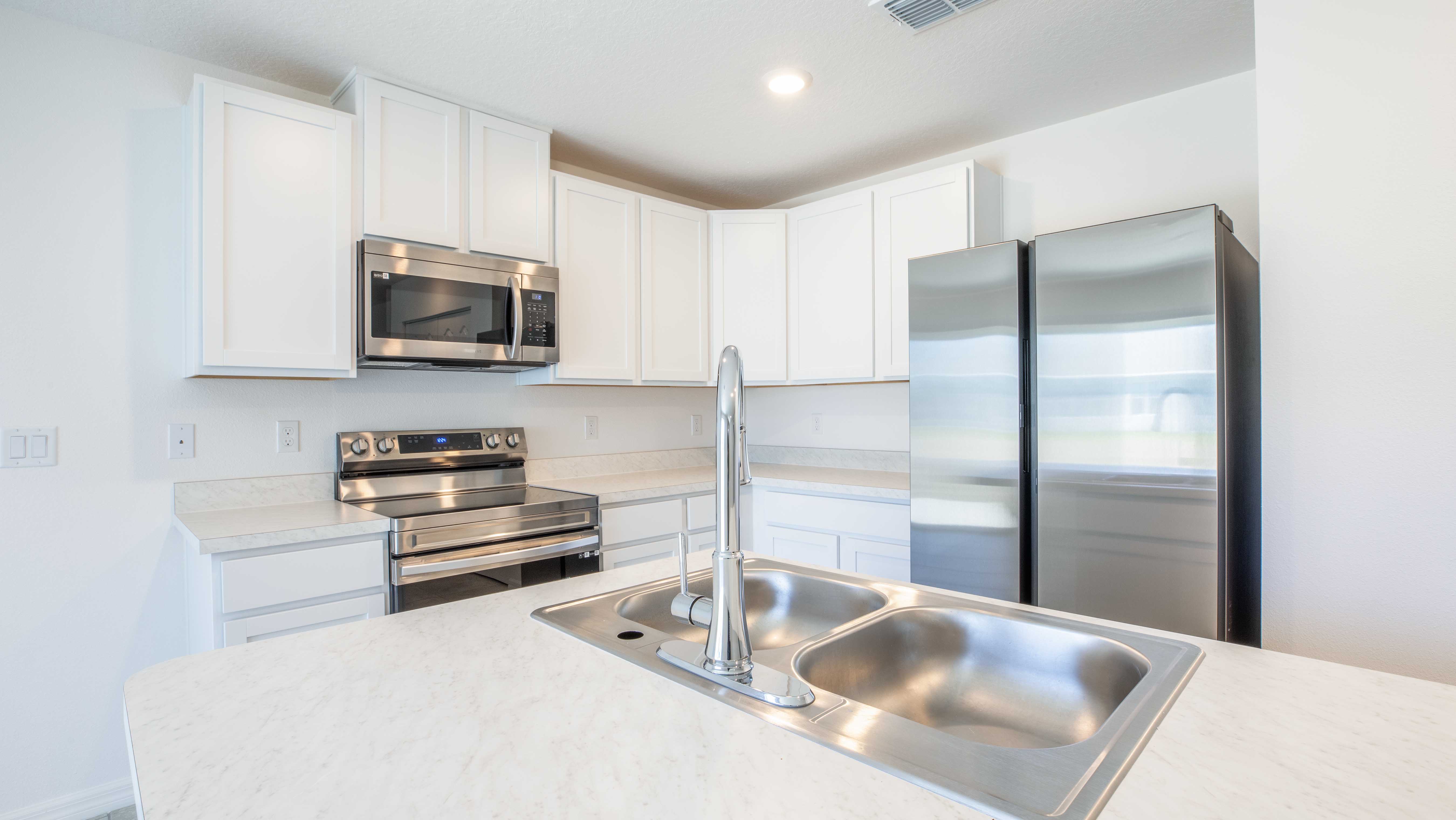 Modern kitchen with stainless steel appliances, white cabinets, and a marble countertop with a dual sink.