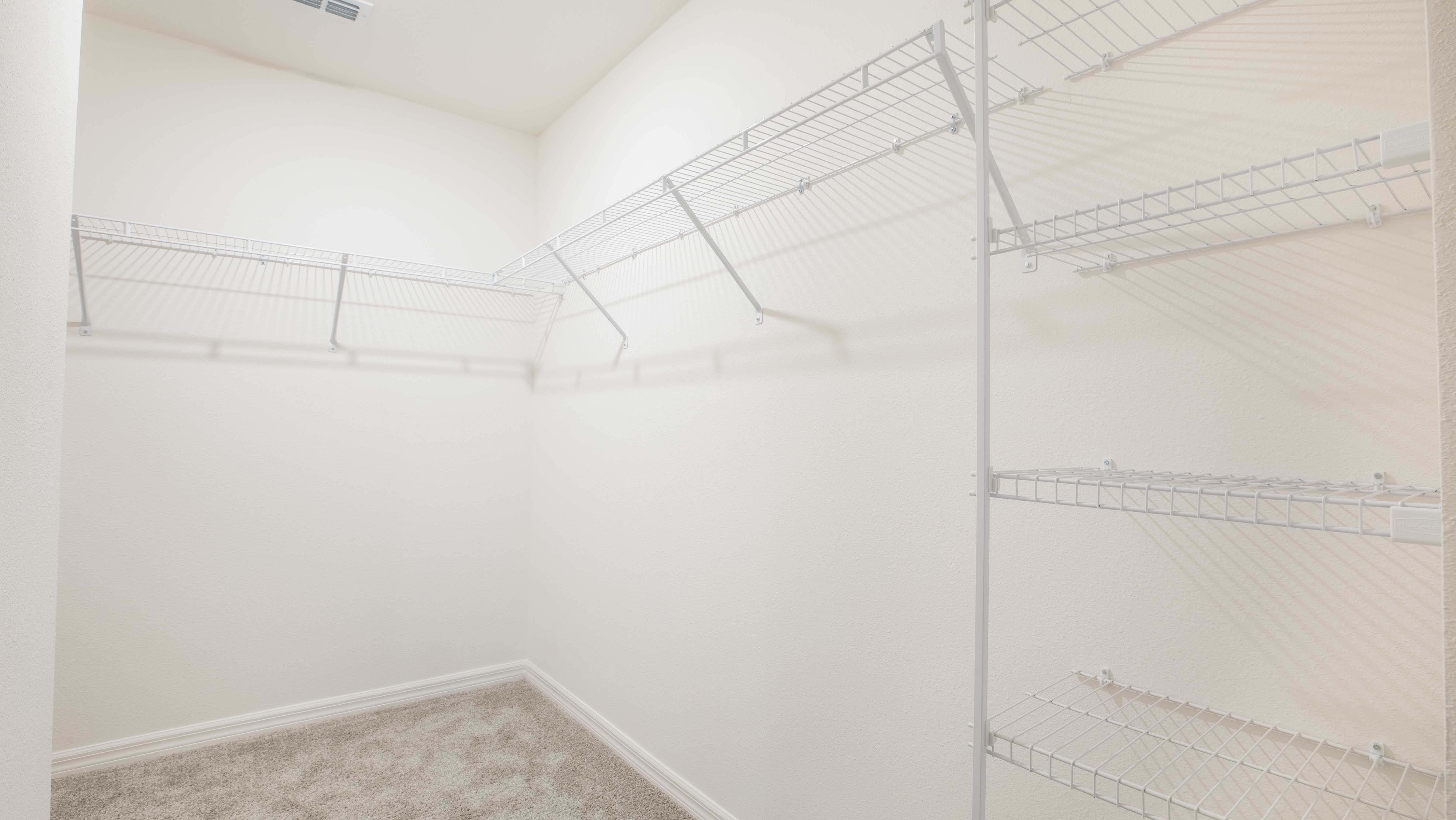 "Spacious empty walk-in closet with white wire shelving and beige walls."