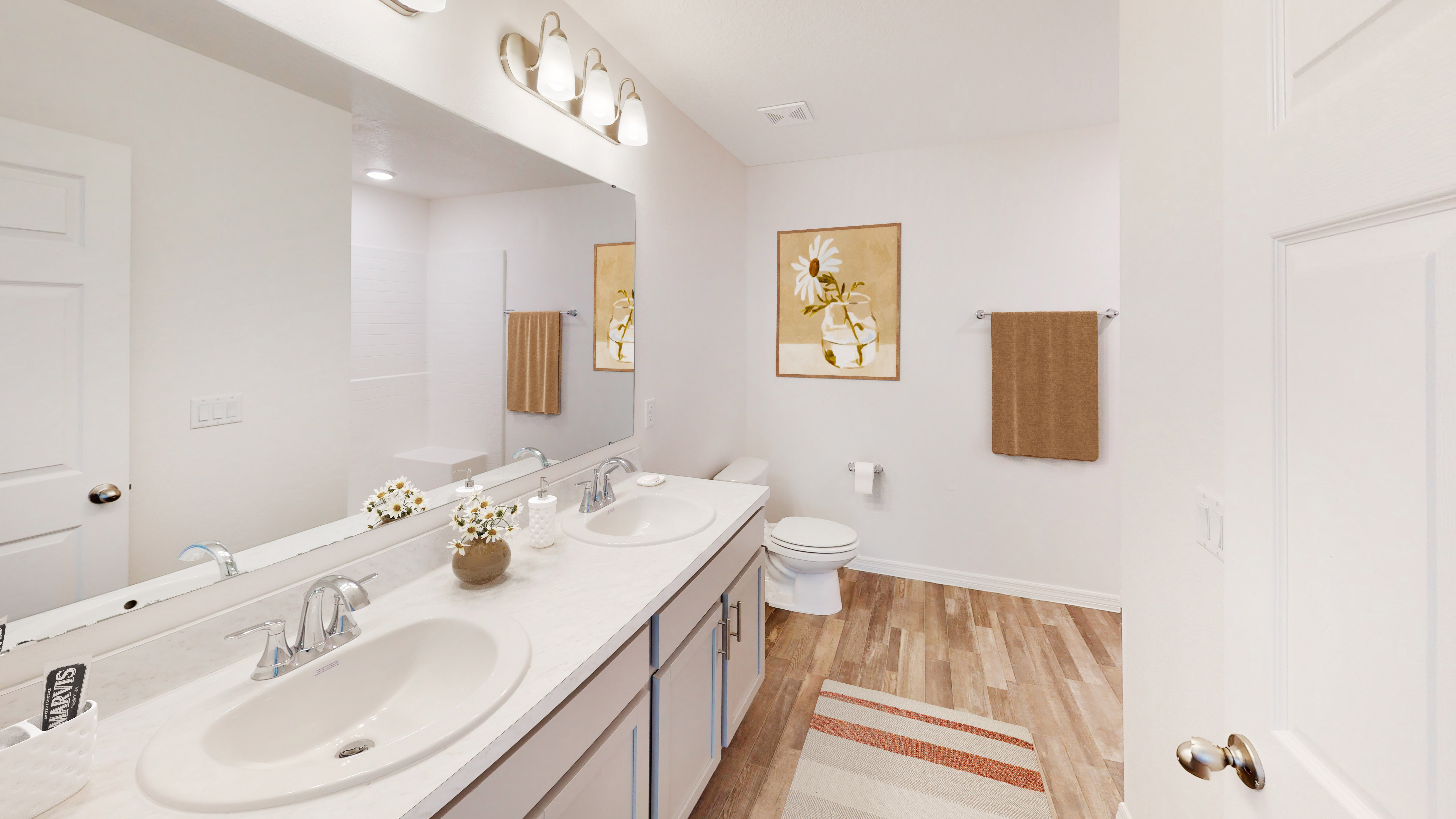 Modern bathroom with a double-sink vanity, wood flooring, and warm-toned decor accents.