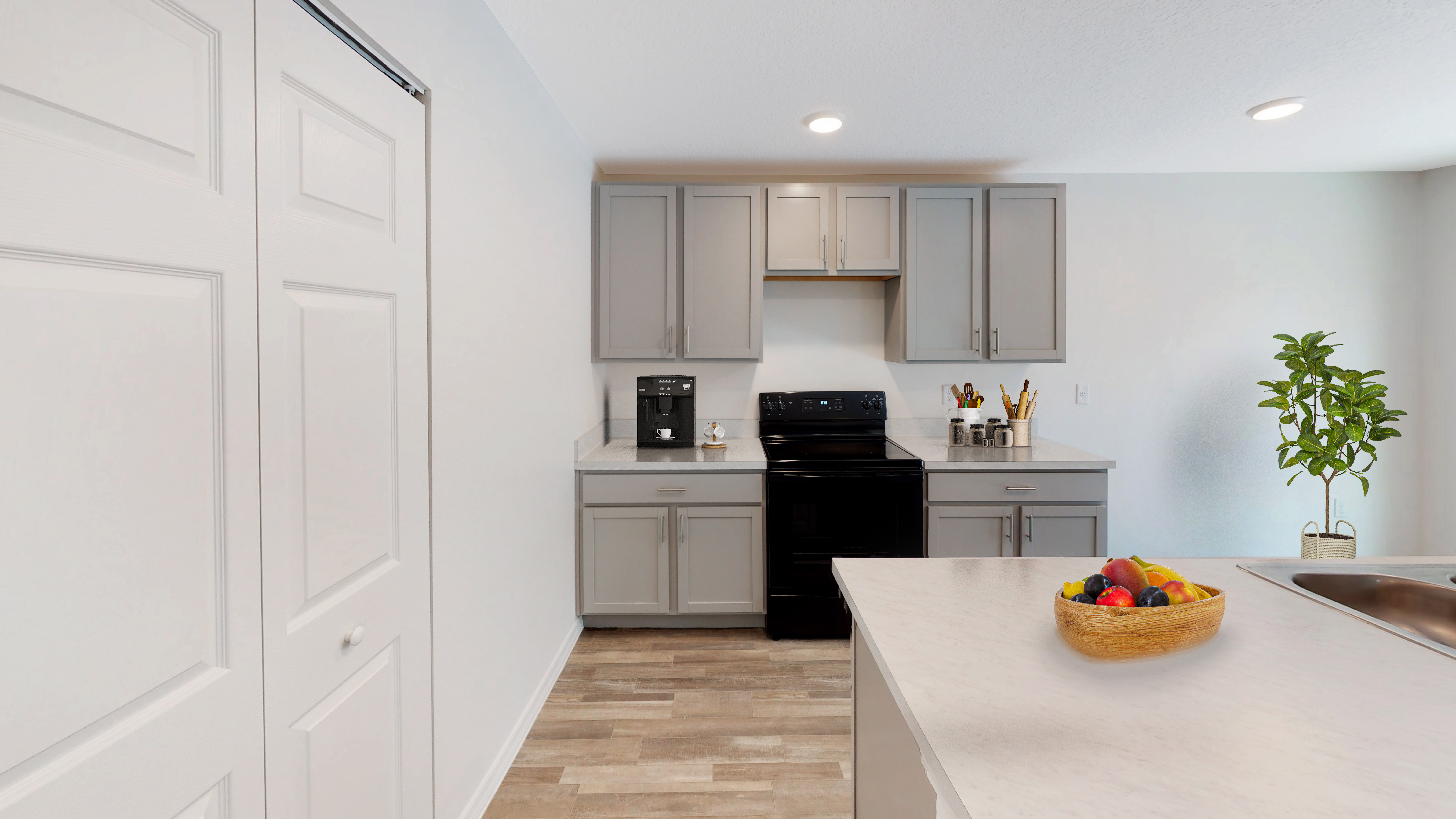 Modern kitchen with gray cabinets, black appliances, and a white countertop featuring a wooden bowl of fruit.