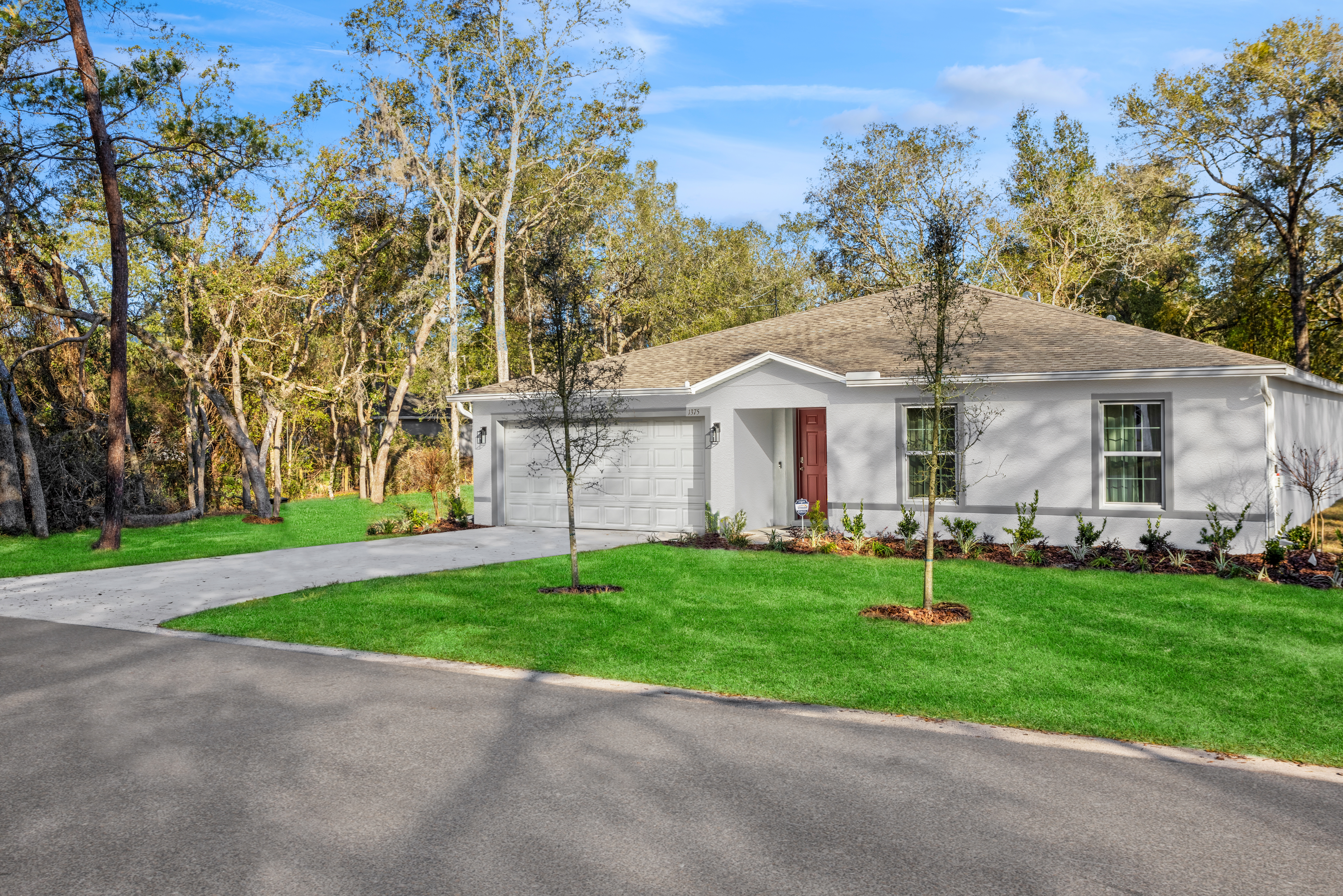 Single-story white house with a red door, attached garage, and manicured lawn surrounded by trees.