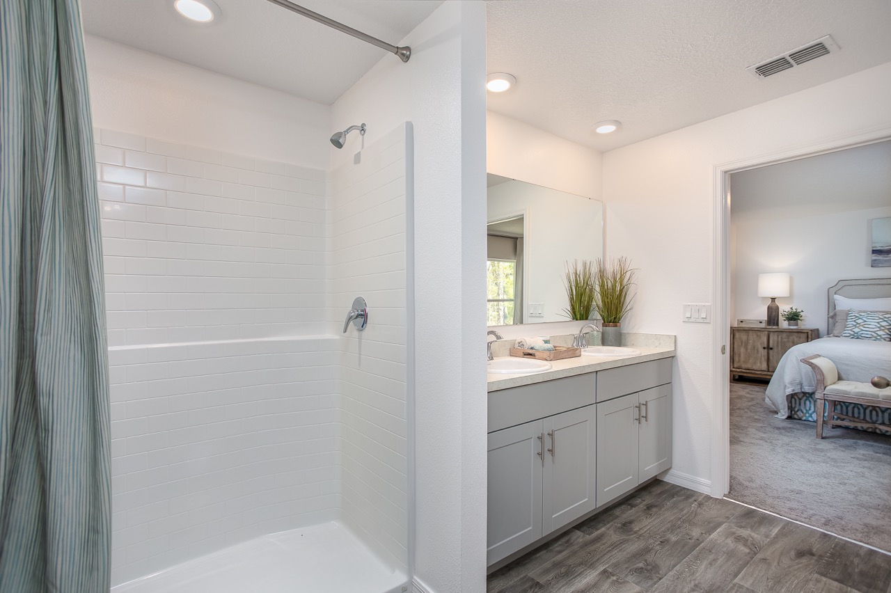 Modern bathroom featuring a spacious walk-in shower, dual-sink vanity, and view into a cozy, well-decorated bedroom.