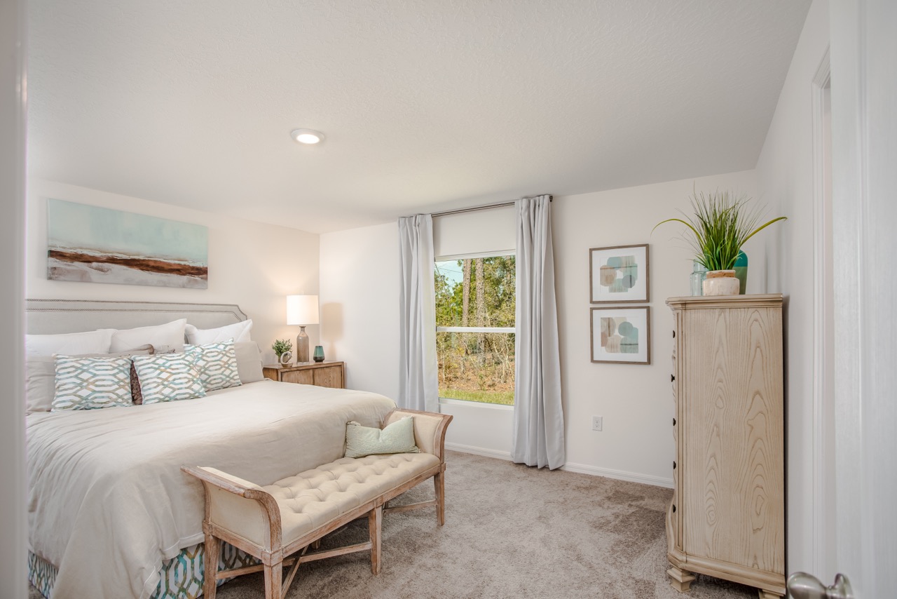 Modern, cozy bedroom with neutral tones featuring a king-sized bed, stylish bench, decorative artwork, and large window.
