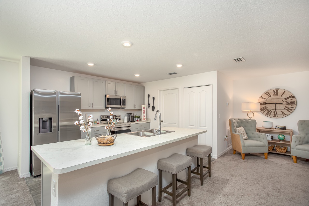 Modern kitchen and cozy seating area with light gray cabinets, a stainless steel refrigerator, and decorative accents.