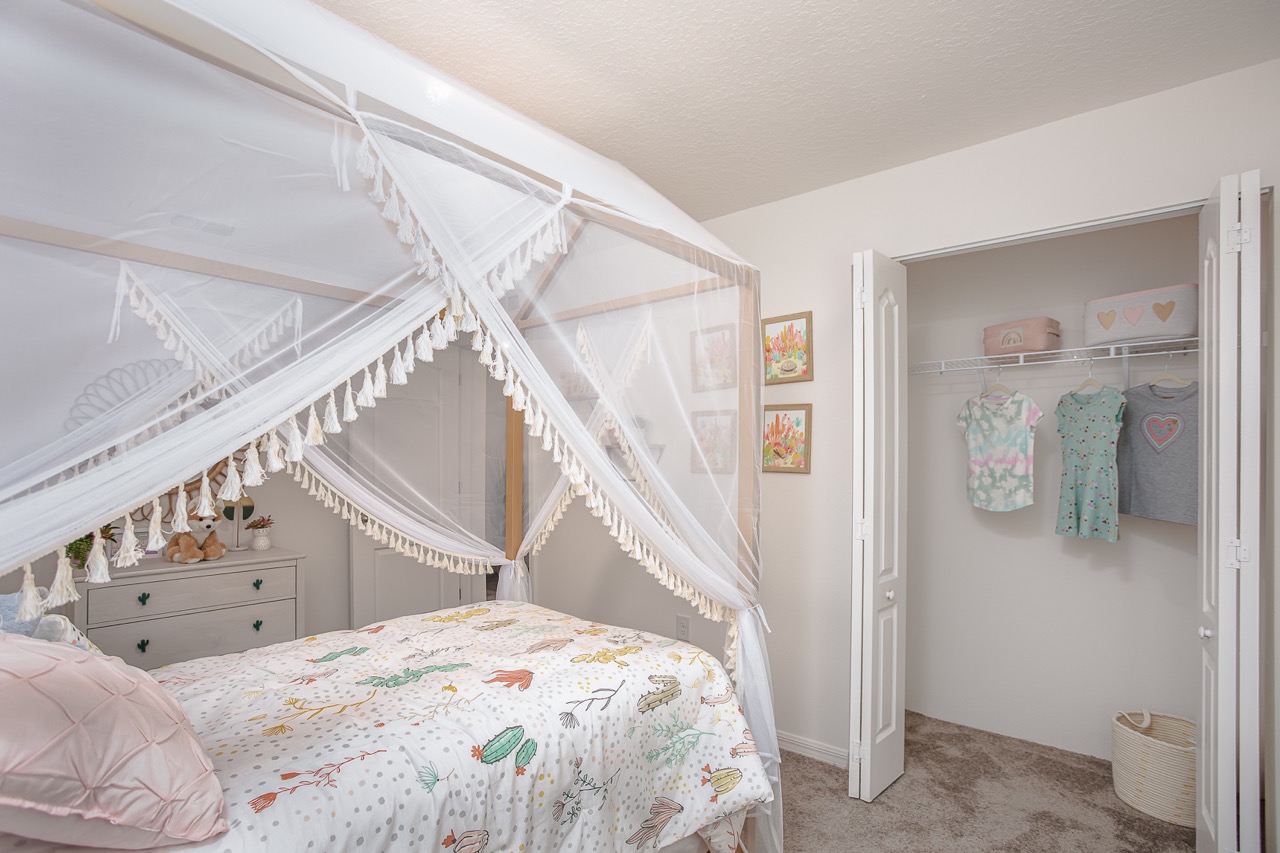 Cozy children's bedroom featuring a canopy bed with tassel detailing, colorful bedding, and an open closet displaying neatly hung clothes.