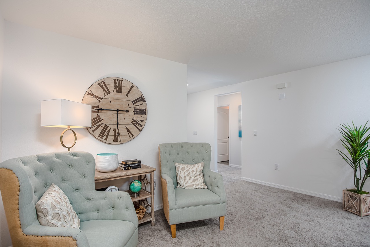 Cozy living room with light green armchairs, a wooden clock, and decorative elements creating a relaxing atmosphere.