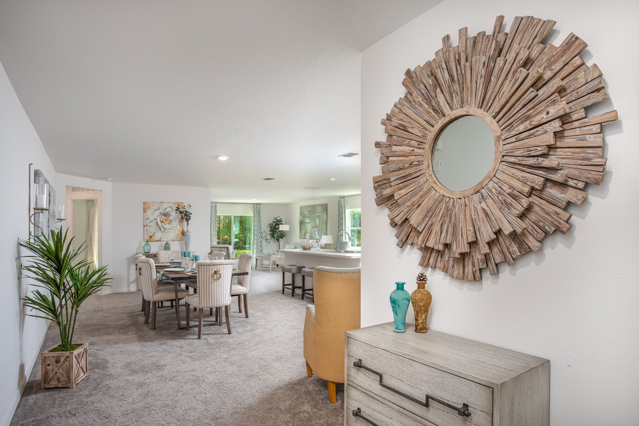 Modern open-plan living and dining area with decorative wooden sunburst mirror and elegant furnishings.