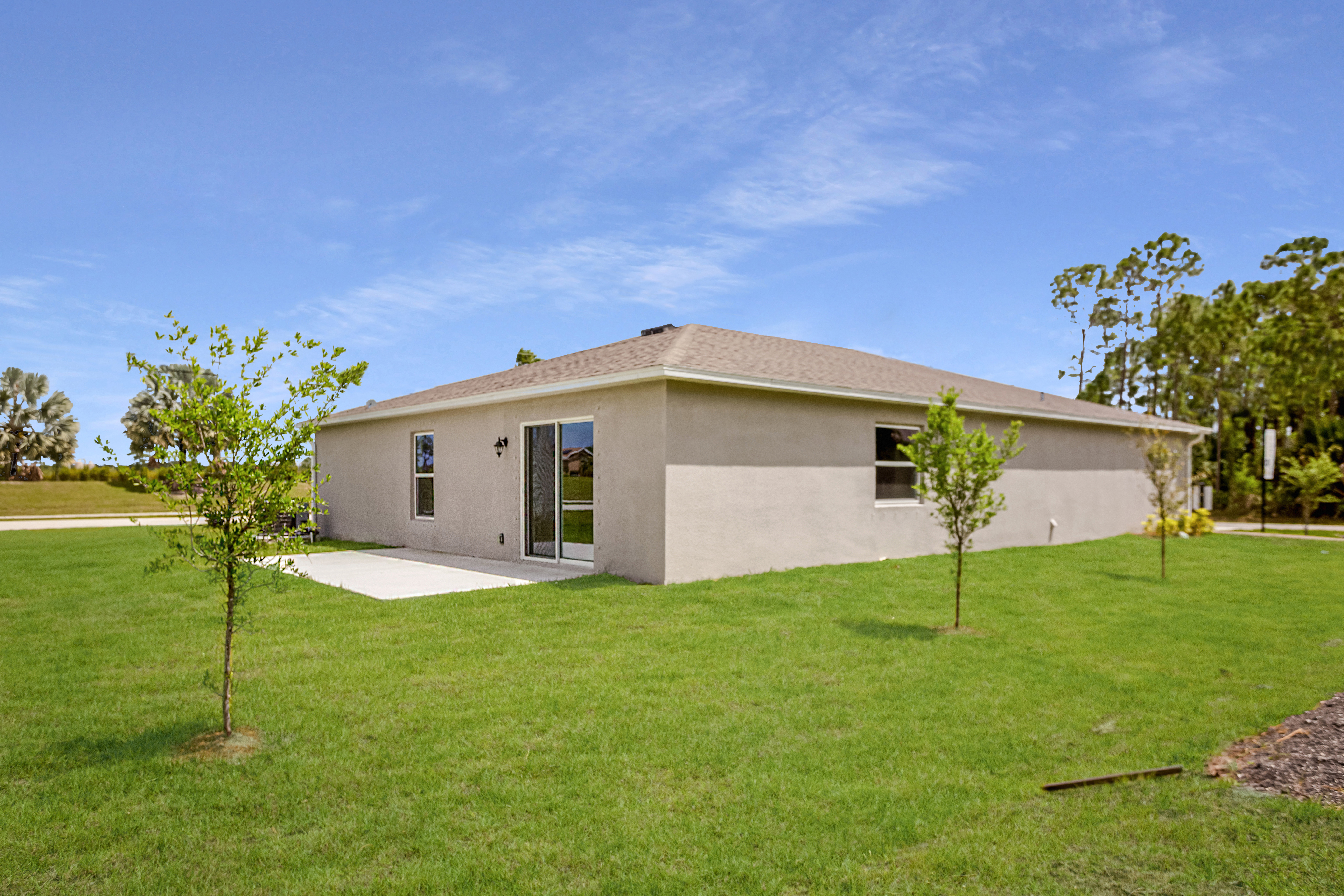 Alt tag: "Modern single-story house with beige exterior and spacious green lawn under a clear blue sky."