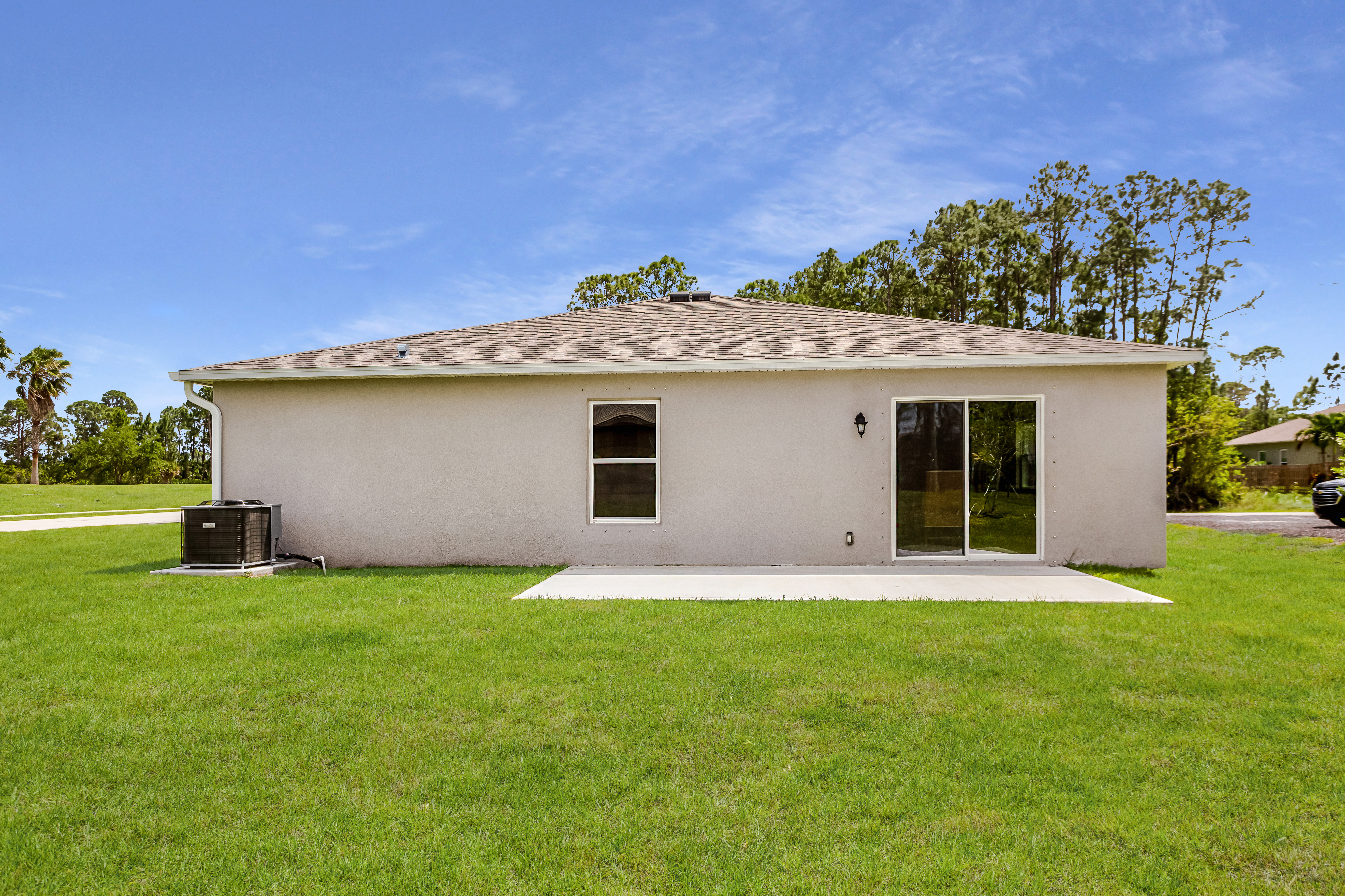 Rear view of a single-story house with a sliding glass door, central air conditioning unit, and a well-maintained lawn.