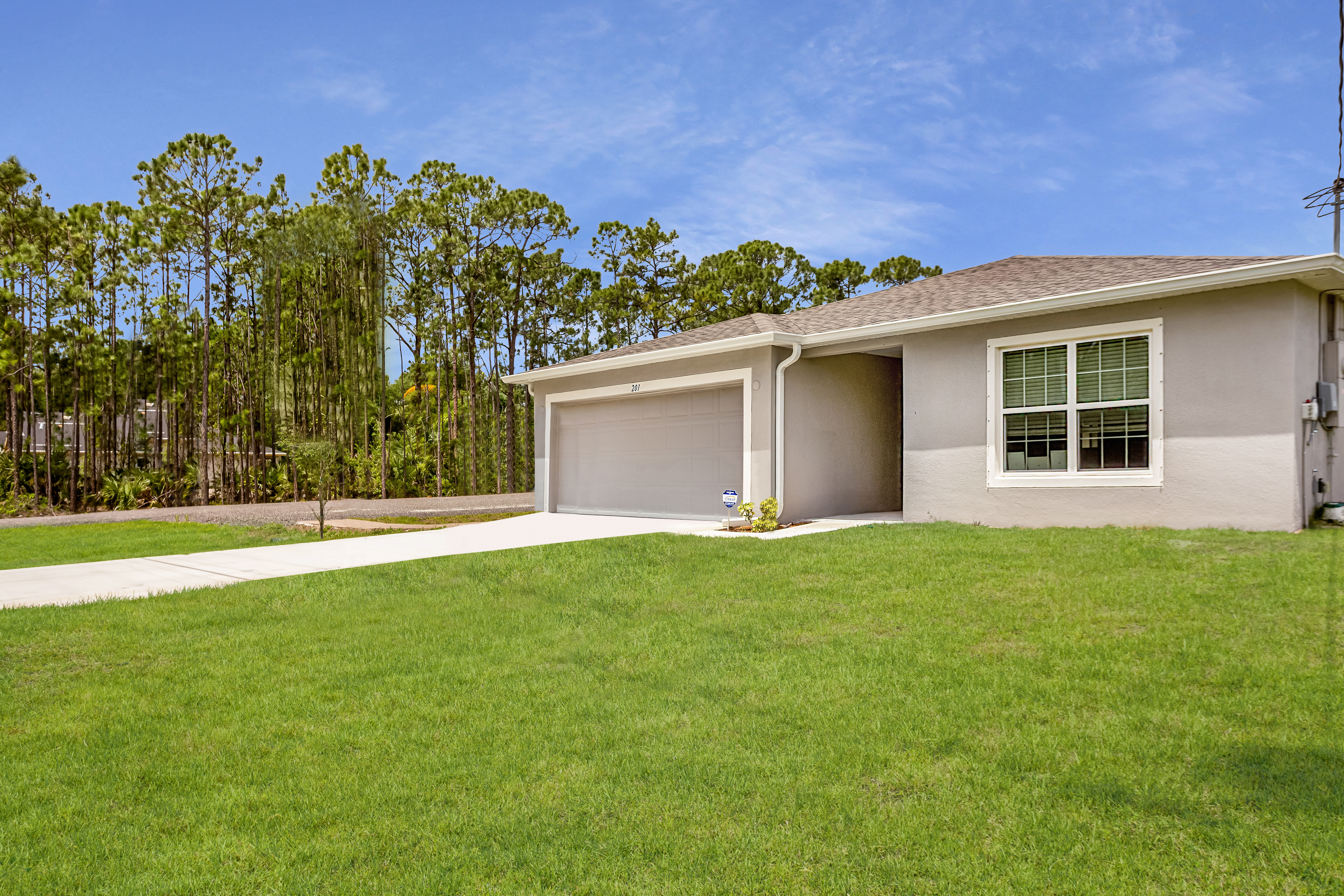 "Modern single-story home with a spacious green lawn and attached garage set against a backdrop of tall trees."