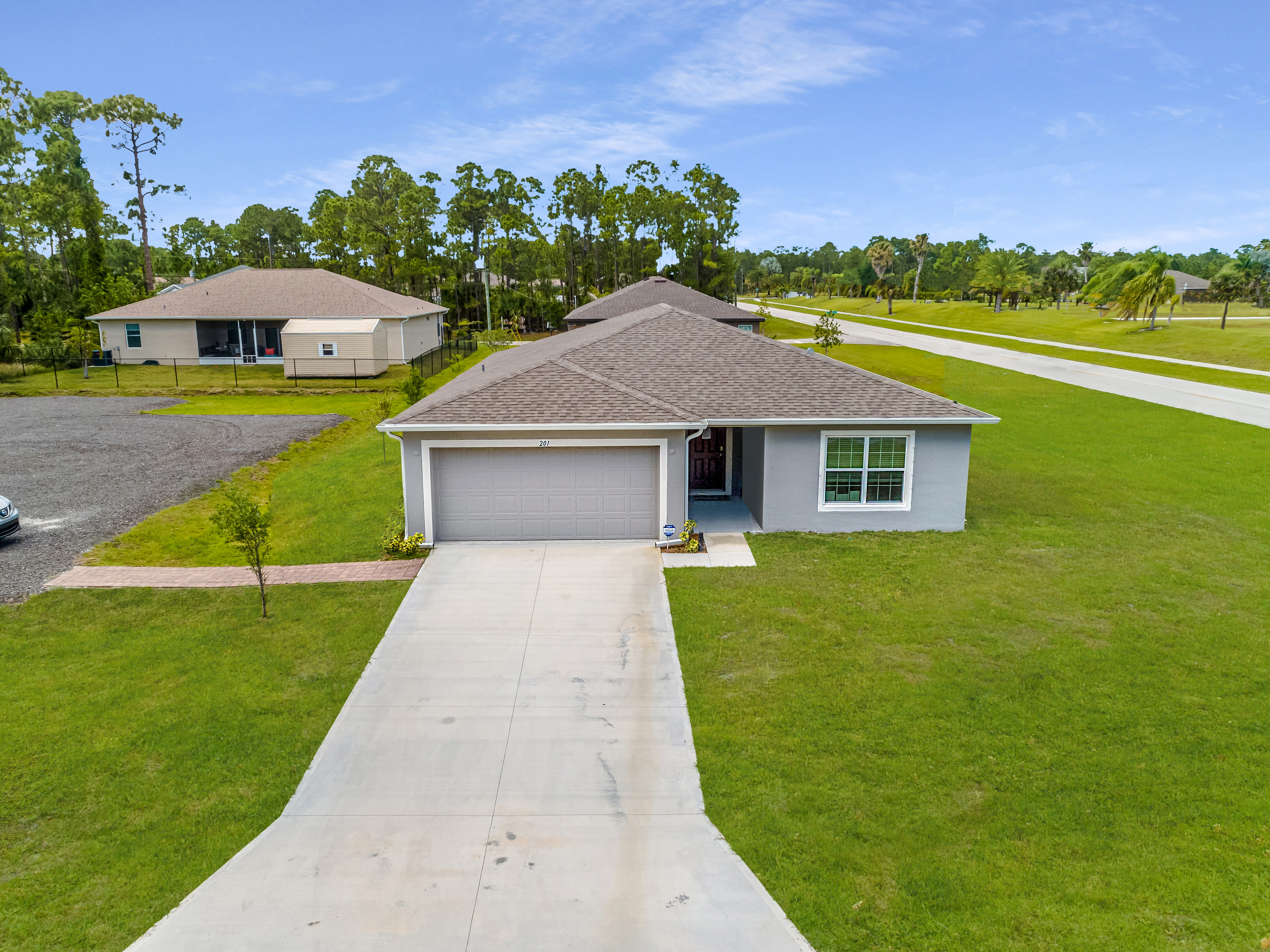 Aerial view of a modern suburban single-story home with a two-car garage, large green lawn, and surrounding trees.