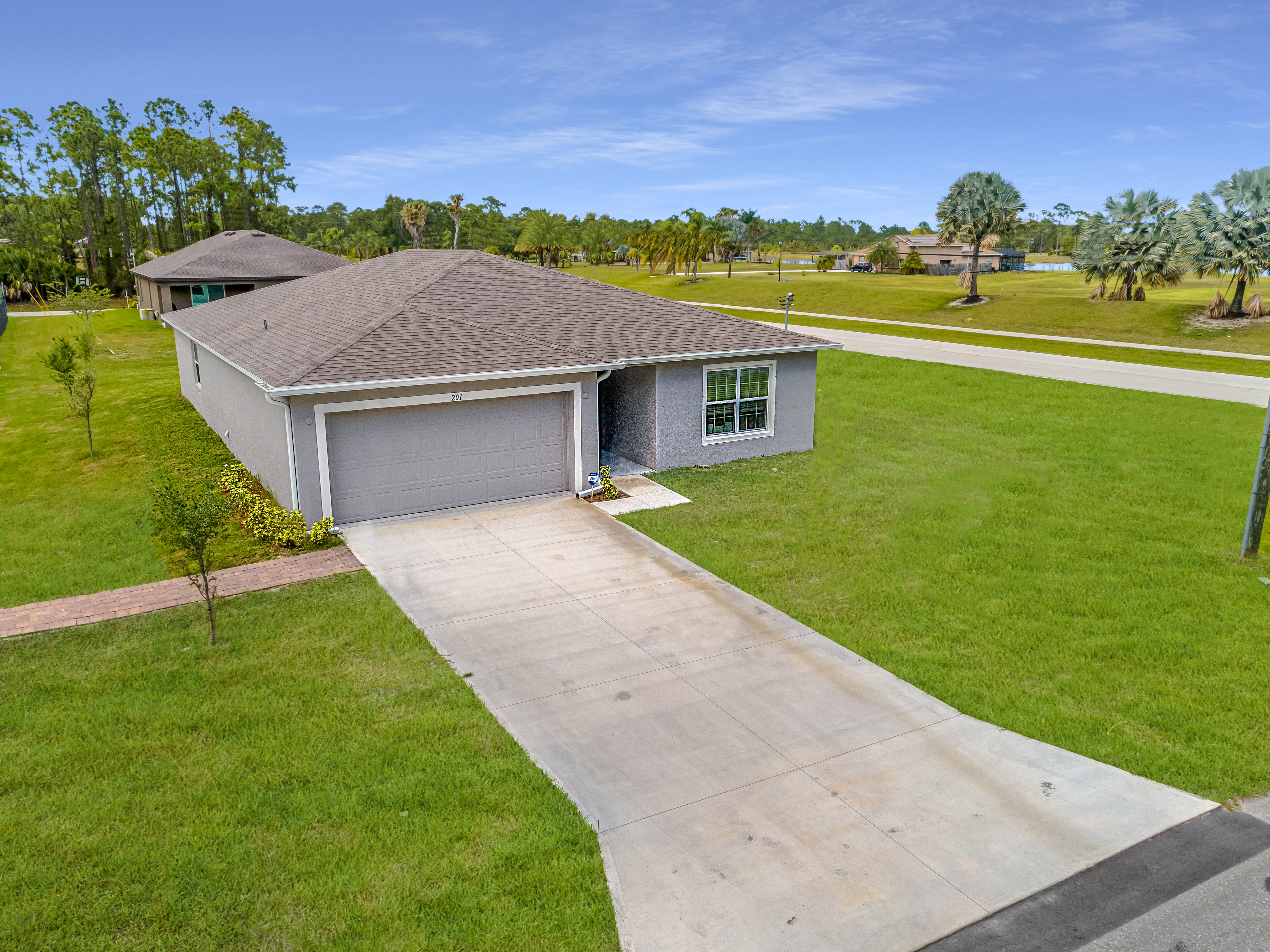 Aerial view of a single-story suburban house with a two-car garage, wide driveway, and well-maintained lawn in a residential neighborhood.