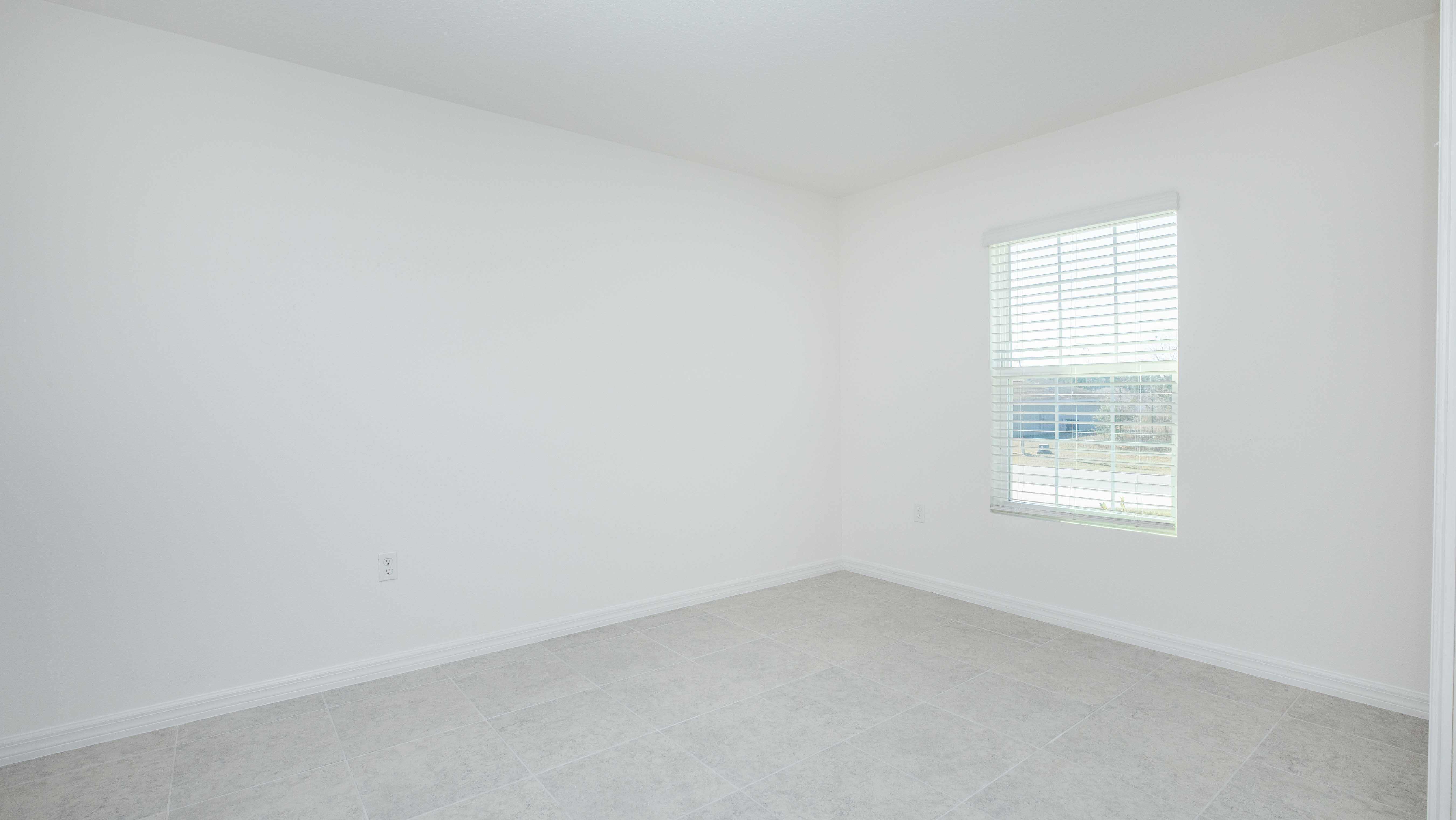 Empty white room with large window featuring closed blinds, tiled floor, and bright natural light.