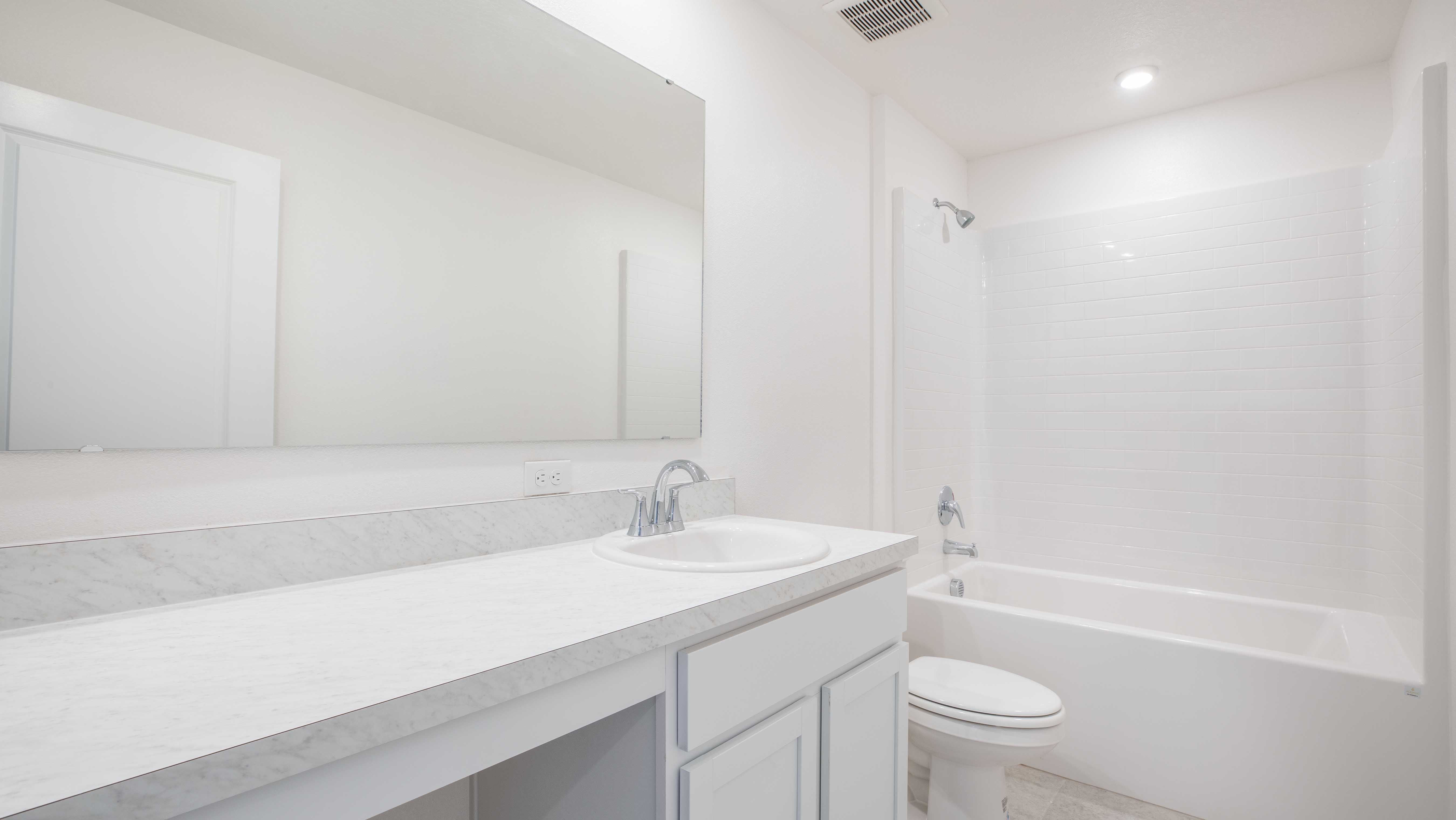 Minimalist white bathroom with a spacious mirror, marble countertop, sink, toilet, and tiled shower-bath combo.