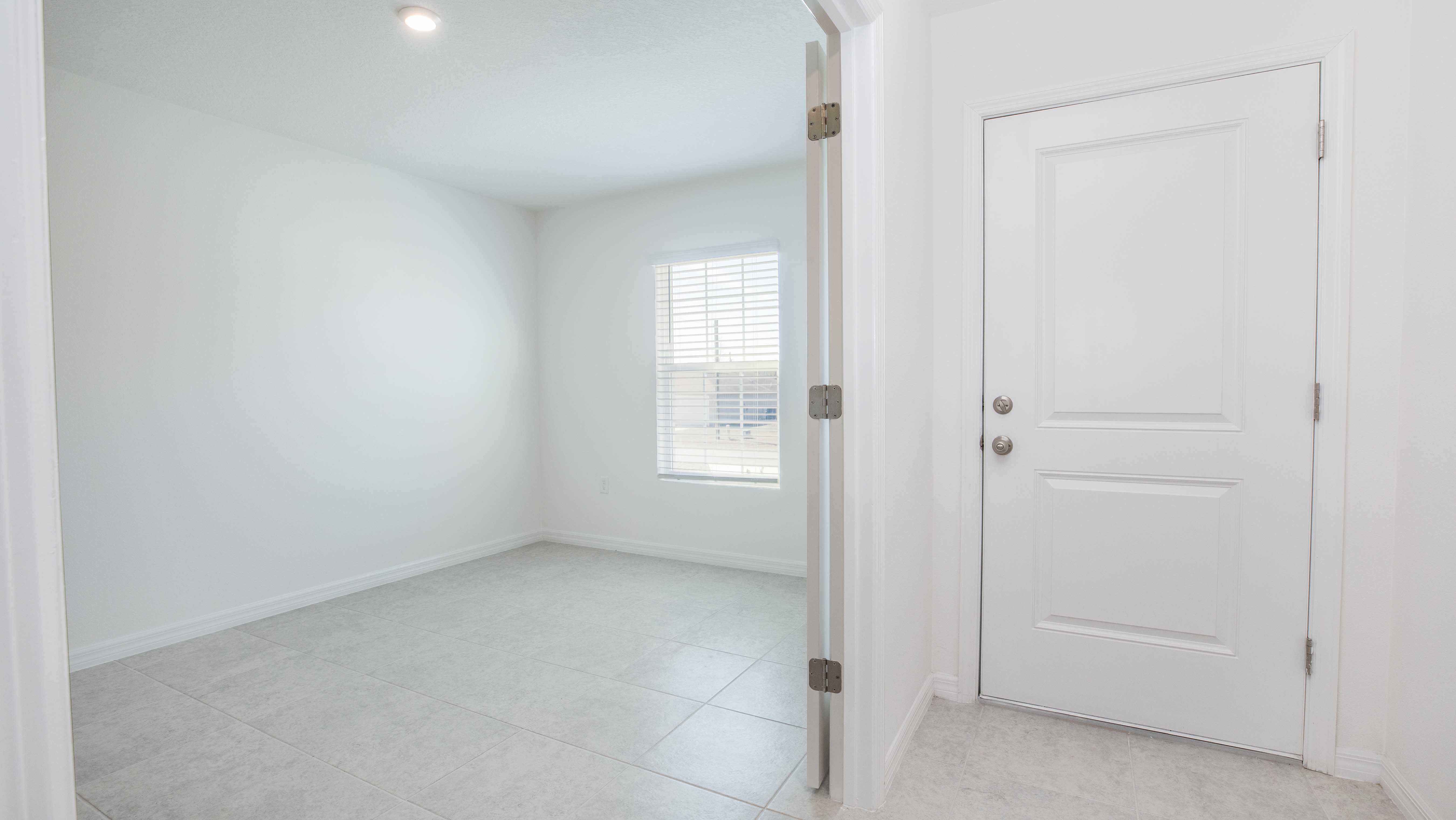 Bright, empty room with tiled floor, white walls, and a door with natural light from a window.