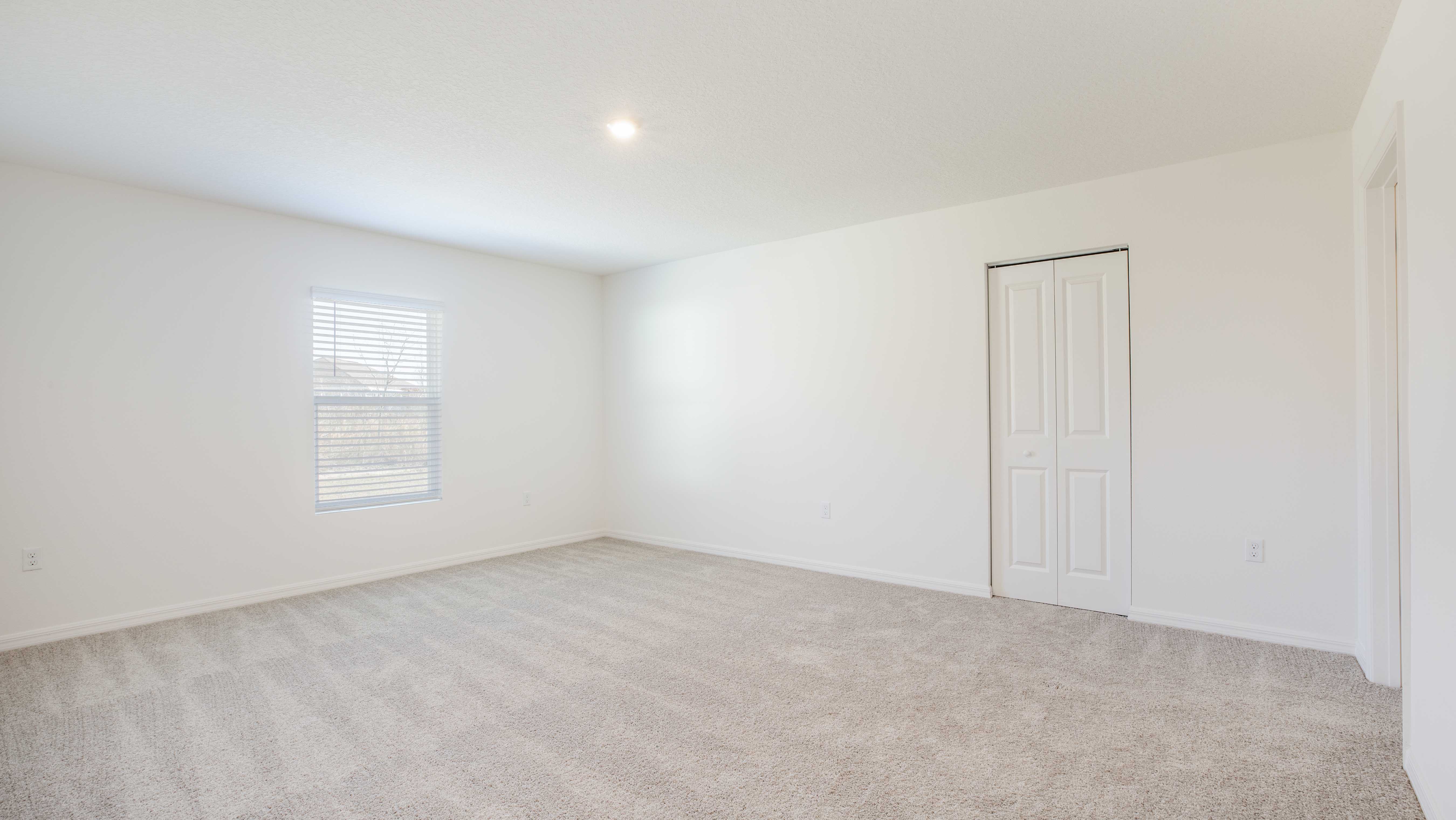 Empty room with beige carpeting, white walls, a window with blinds, and a closed closet door.