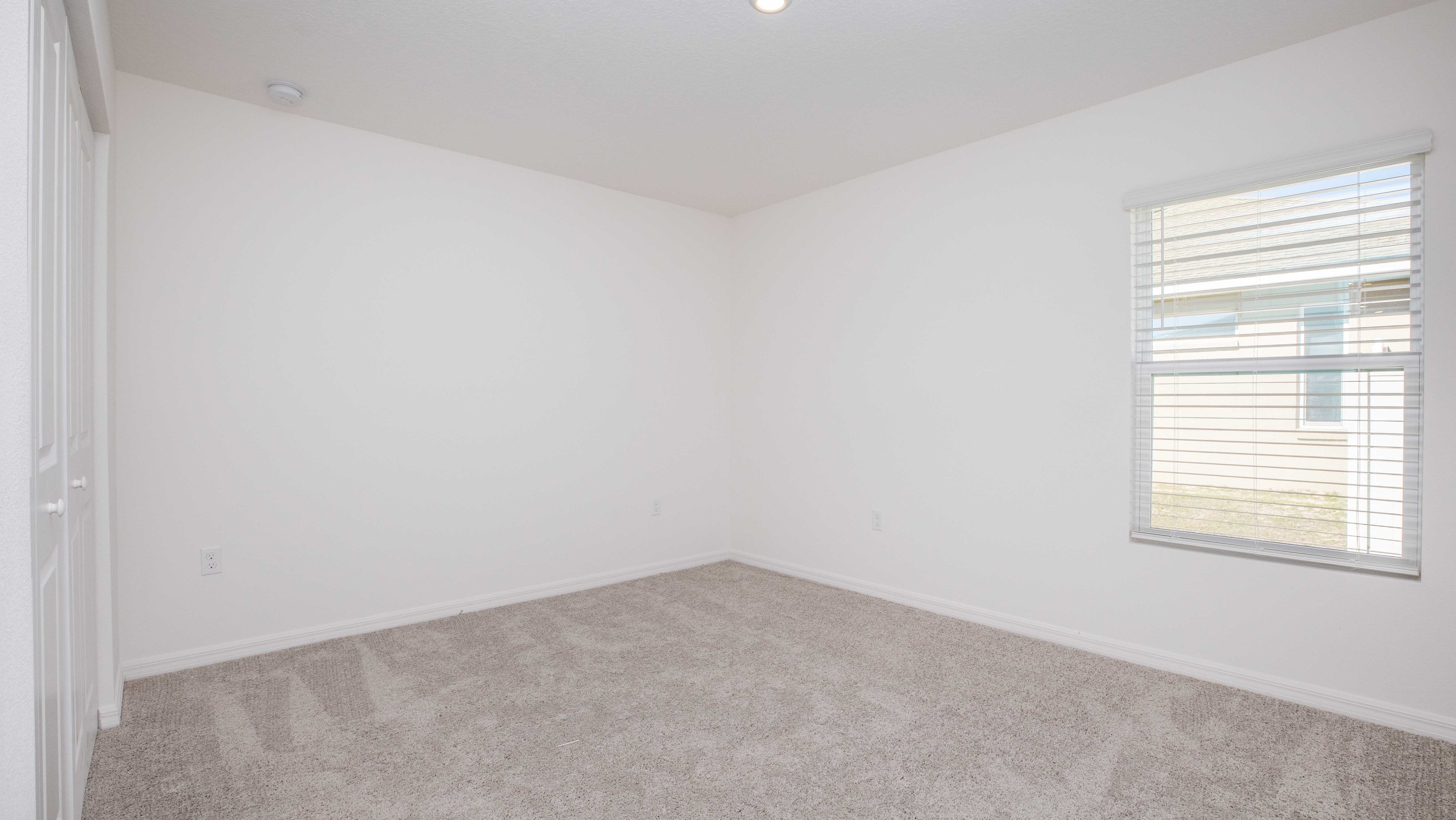 Empty room with white walls, carpet flooring, and a window with blinds.